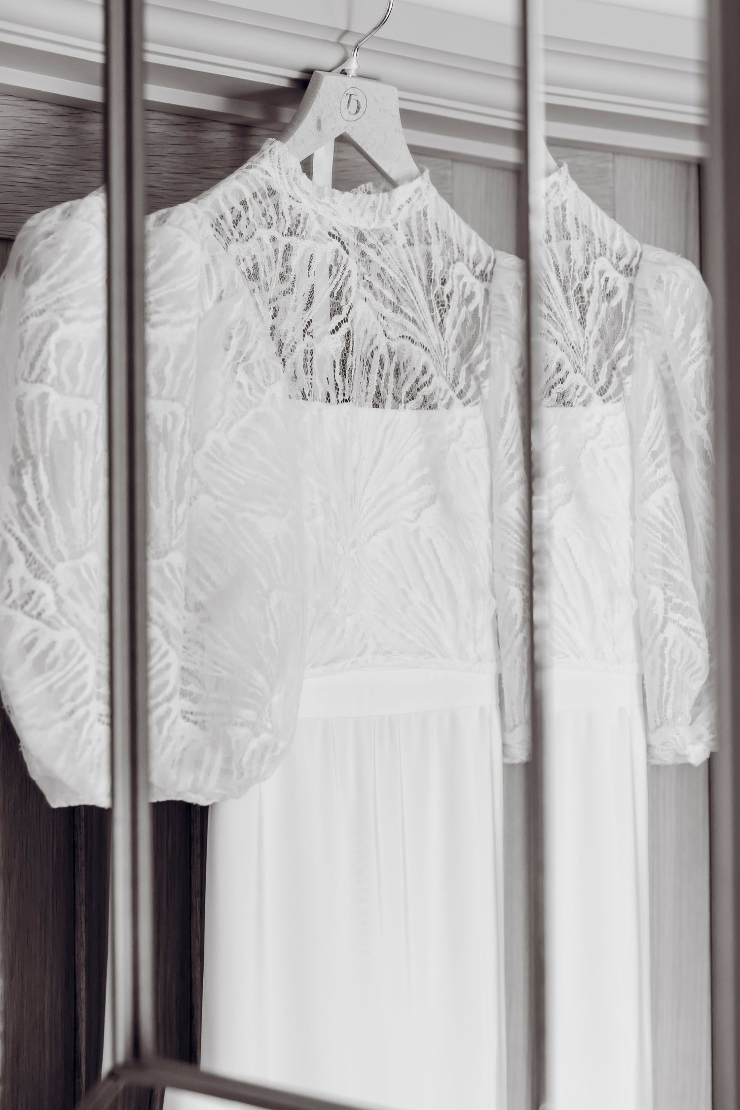 White lace wedding dress with puff sleeves hanging on a hanger reflected in a mirror.