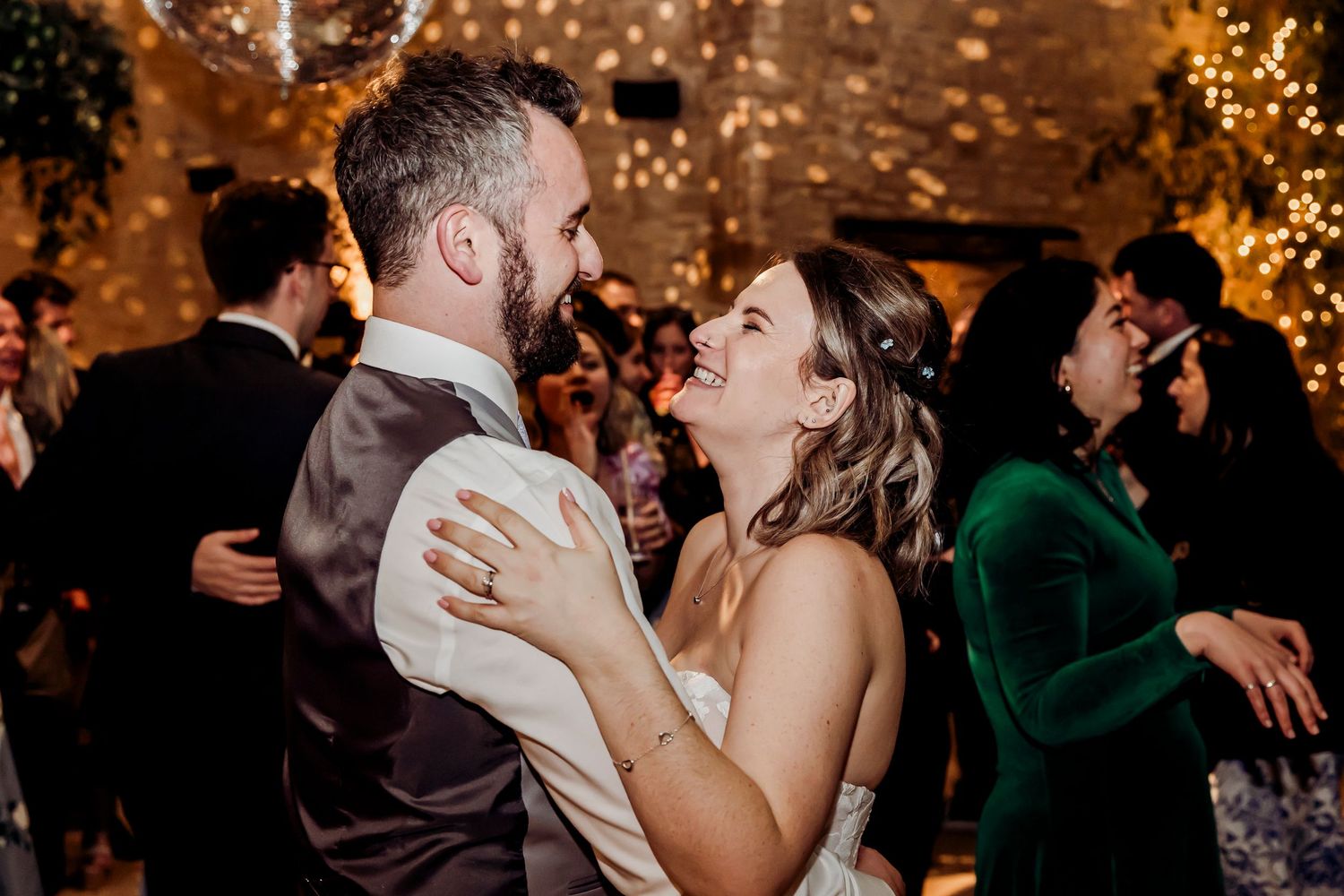 Bride and groom dancing and laughing together under disco ball at wedding reception.