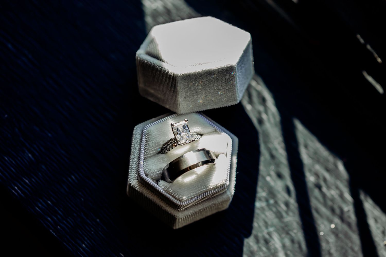 Wedding rings displayed in a hexagonal velvet ring box on a dark surface.