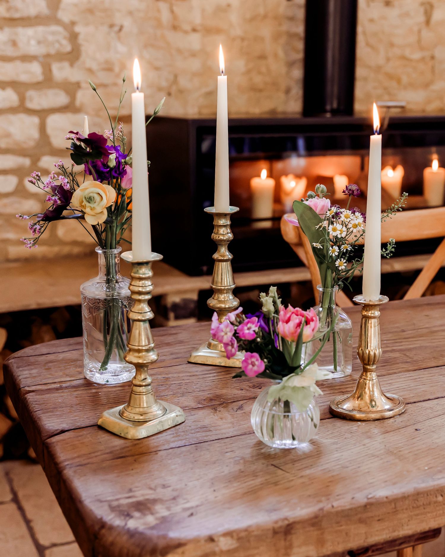 Elegant rustic wedding table with gold candlesticks, white taper candles, and colorful floral arrangements.