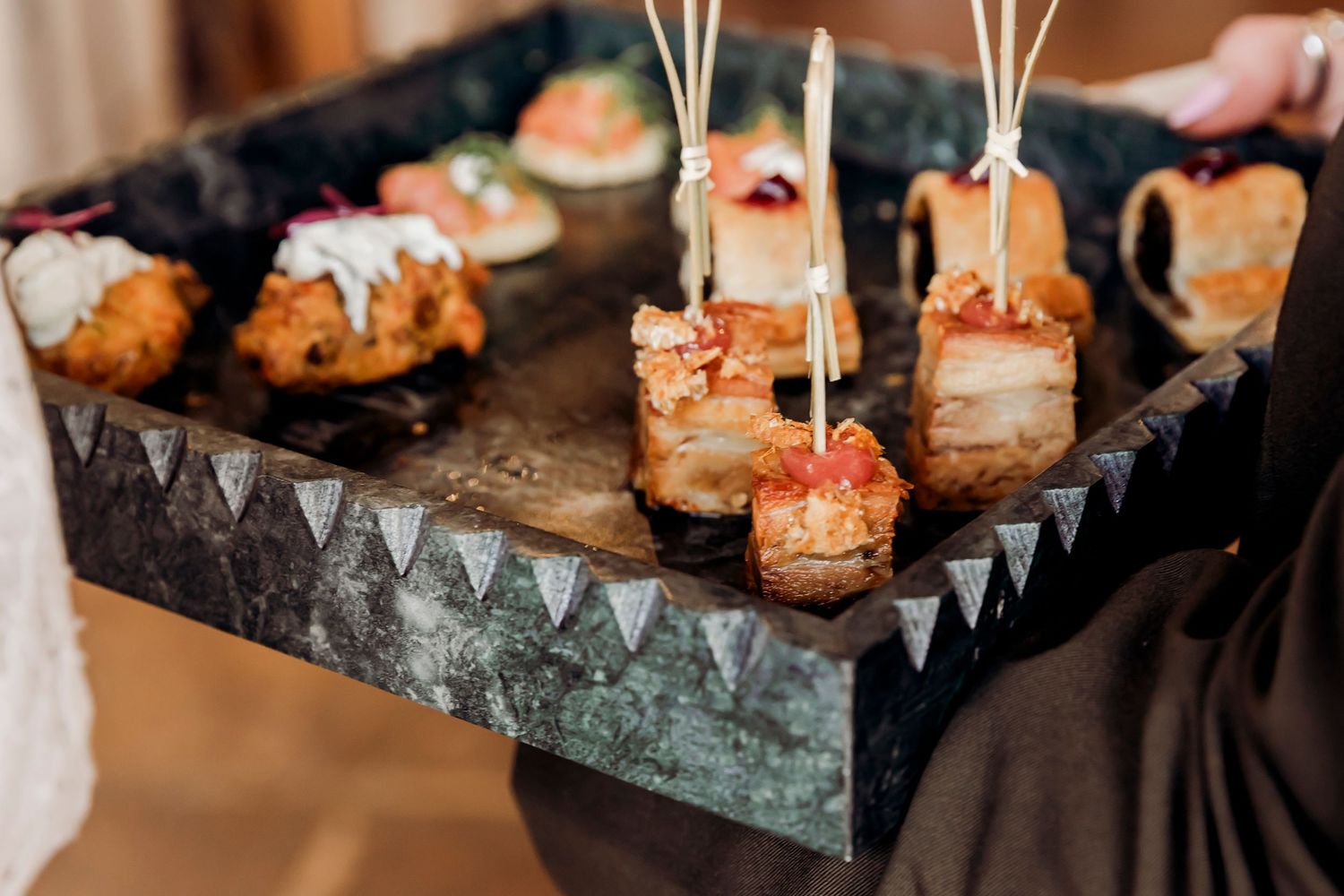 Elegant appetizer tray with bacon-wrapped bites and gourmet canapés served at a catered event.