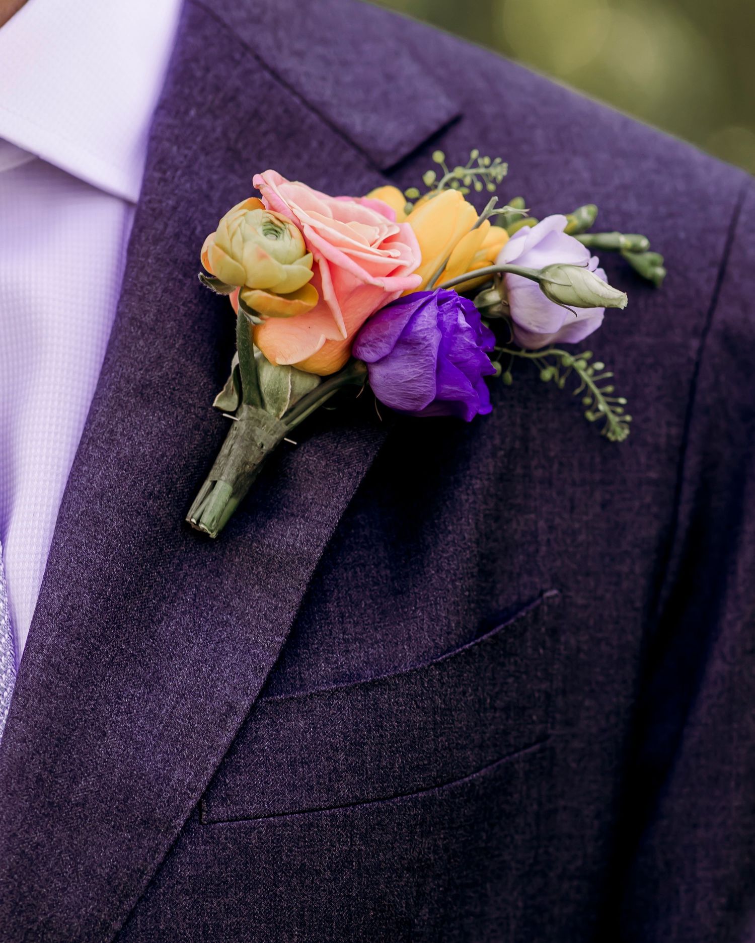 Colorful boutonniere with pink, yellow, and purple flowers on a purple tweed wedding suit lapel.