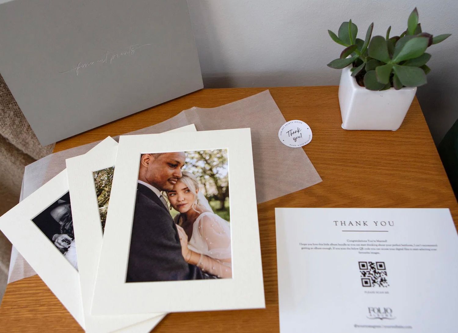 Wedding thank you cards with couple portrait prints displayed on wooden table with plant.