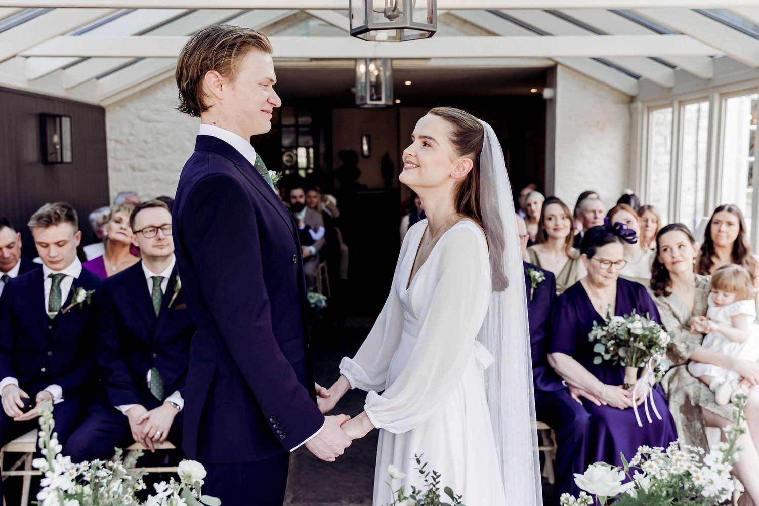 Bride and groom holding hands and smiling at each other at the altar during their wedding ceremony.