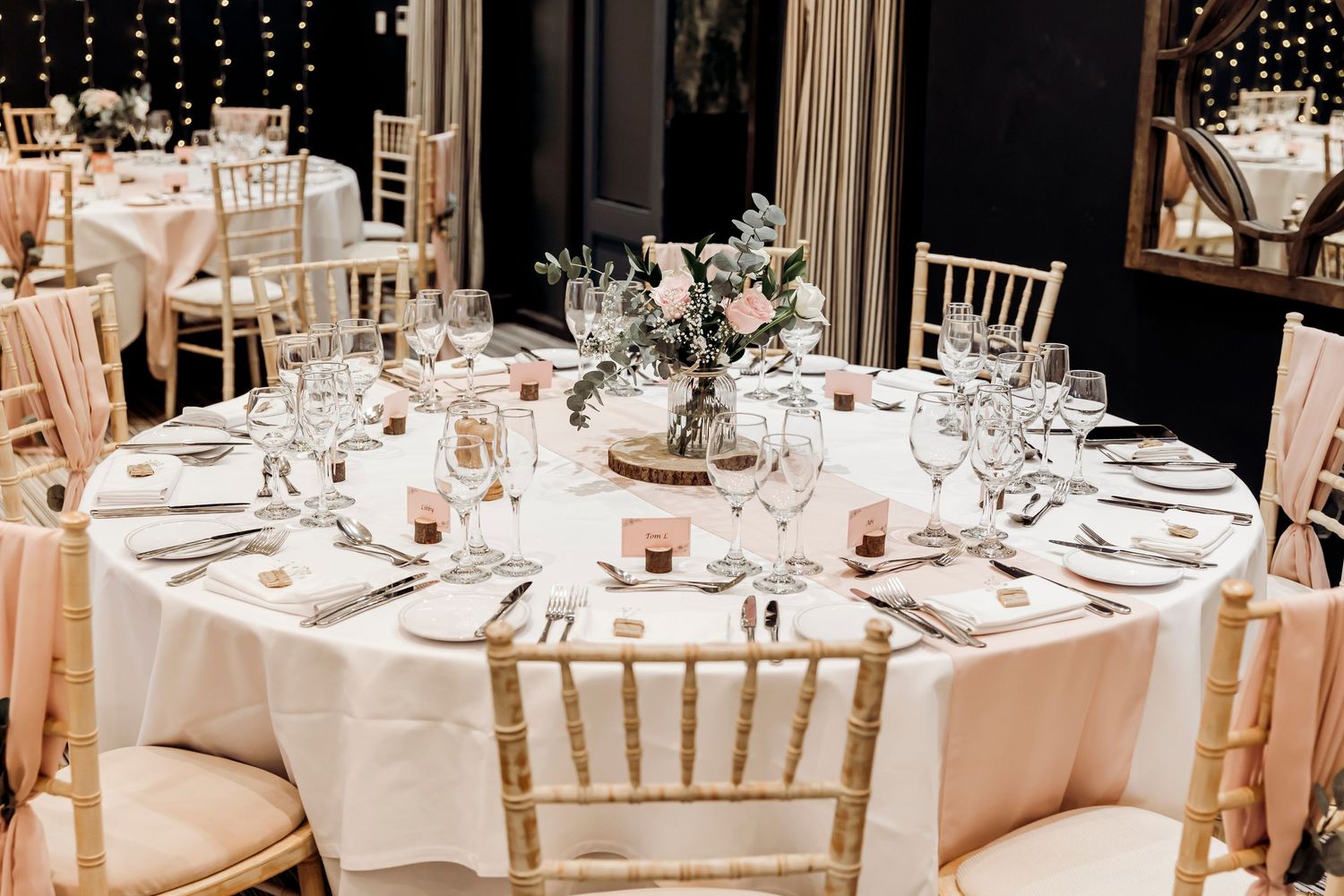 Elegantly set round wedding reception table with gold chiavari chairs, pink linens, and floral centerpiece.