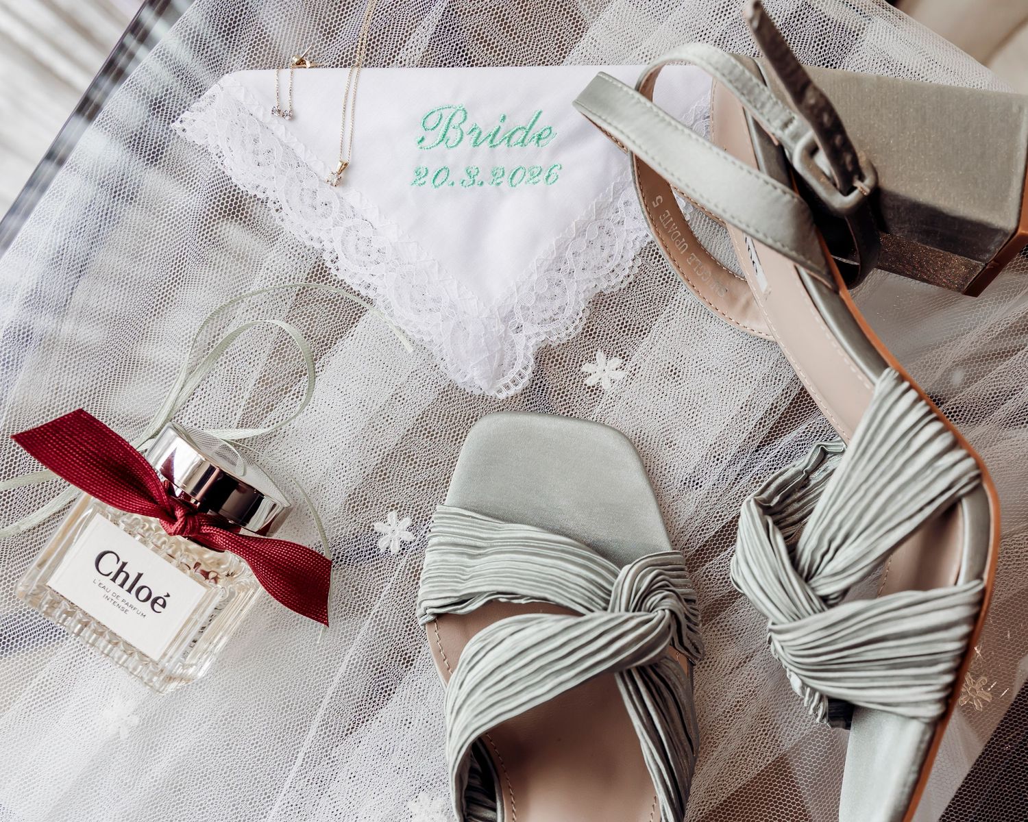 Bridal accessories flat lay featuring sage bow heels, Chloe perfume, and embroidered handkerchief.