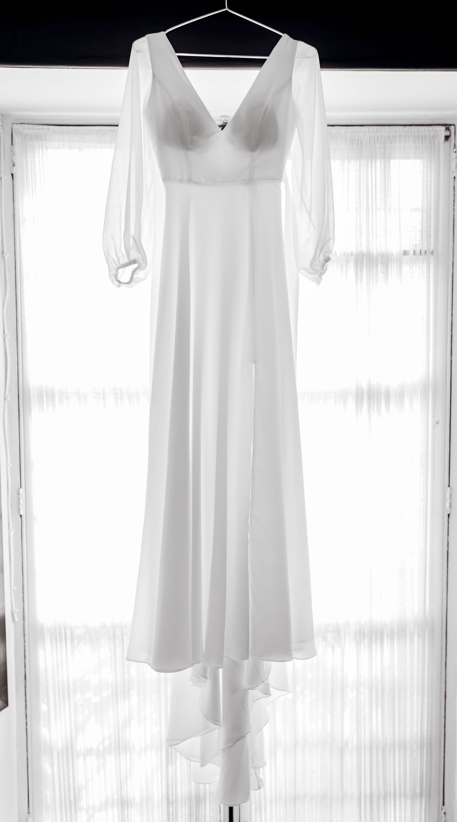 Elegant white V-neck long sleeve wedding dress hanging in window natural light bridal detail.