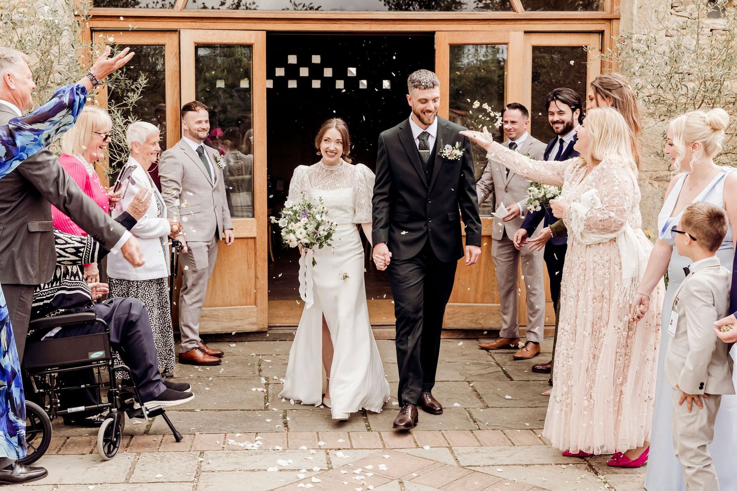Newlyweds walk through confetti shower outside rustic barn wedding venue.