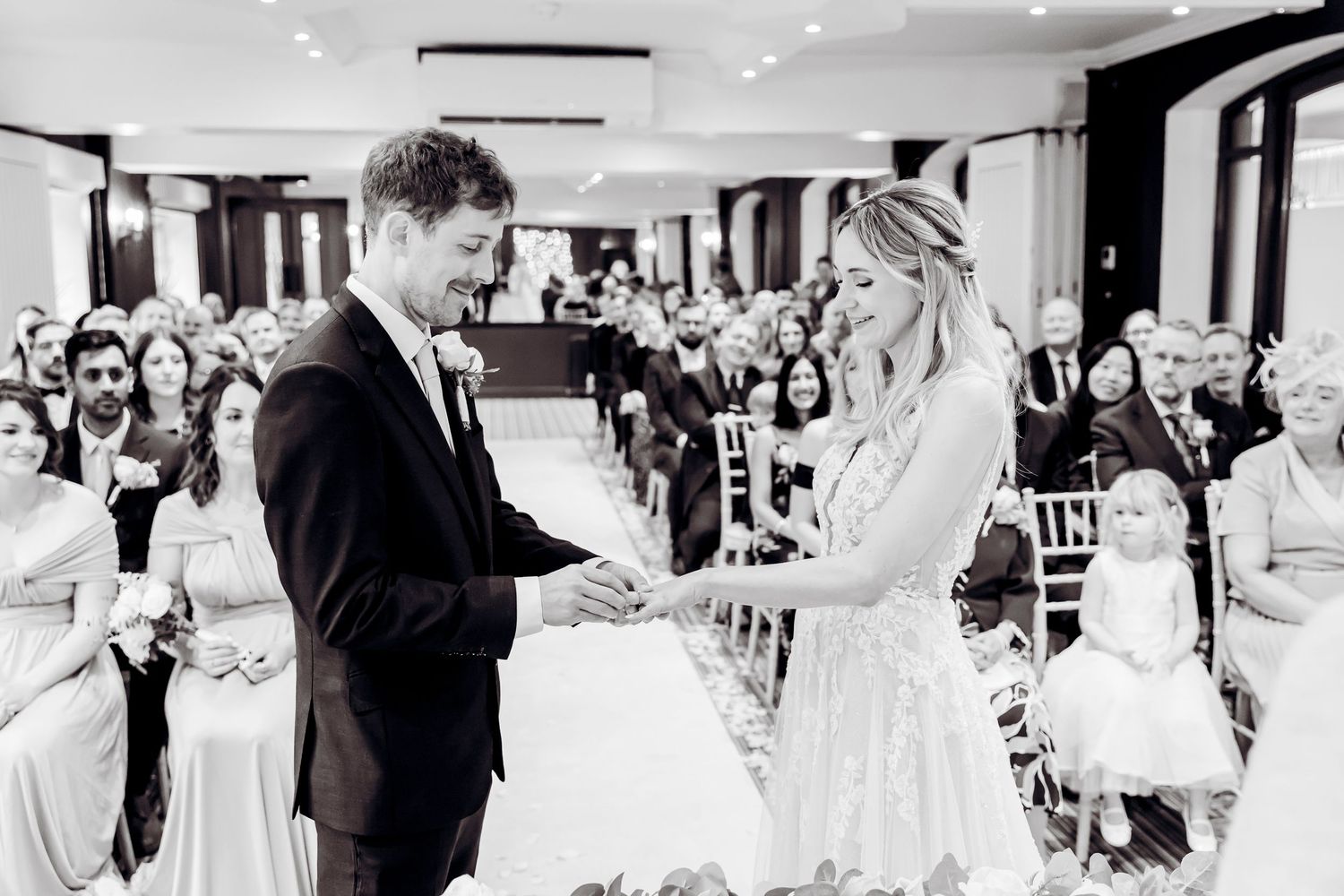 Black and white photo of bride and groom exchanging rings during wedding ceremony.
