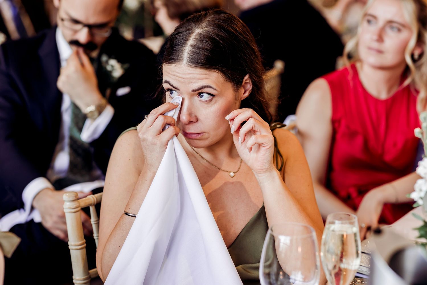 Emotional wedding guest wiping tears during heartfelt wedding speeches at reception.