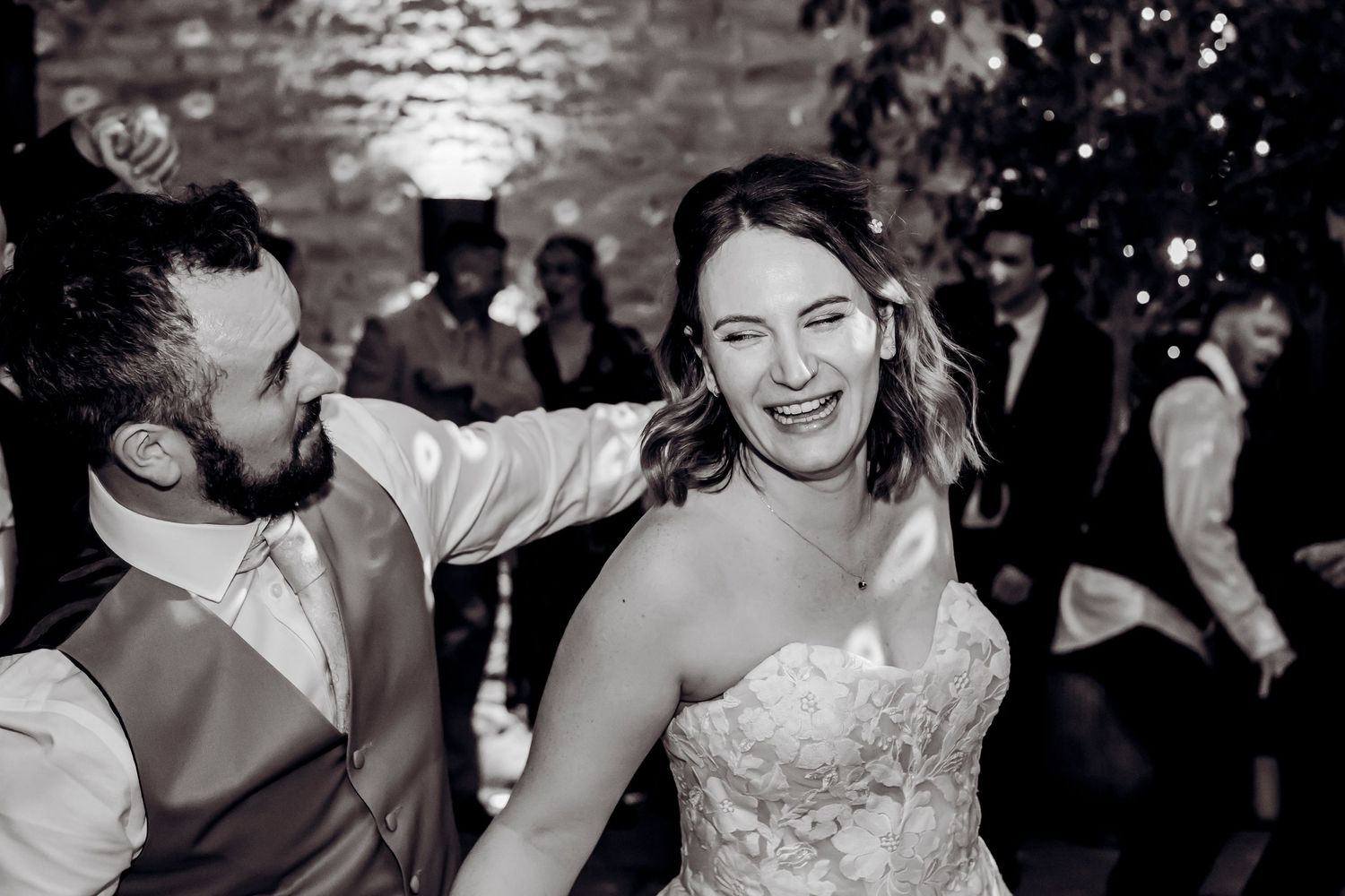 Bride laughing joyfully with groom during lively black and white wedding reception dance.