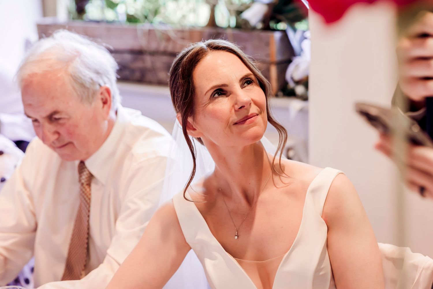 A bride in a white gown gazing thoughtfully during a wedding reception indoors.