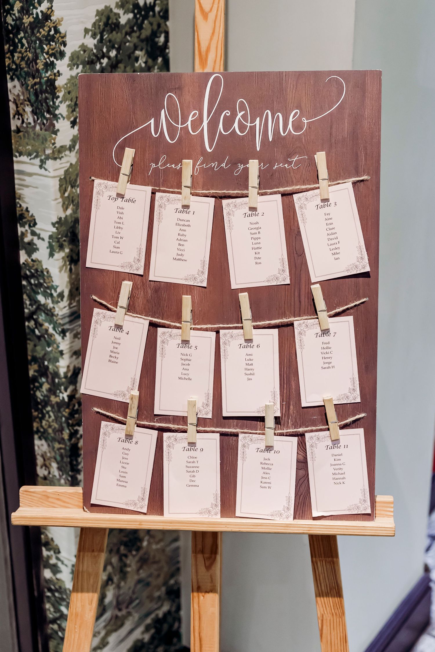 Rustic wooden wedding seating chart display on easel with clothespin-attached table cards reading Welcome.