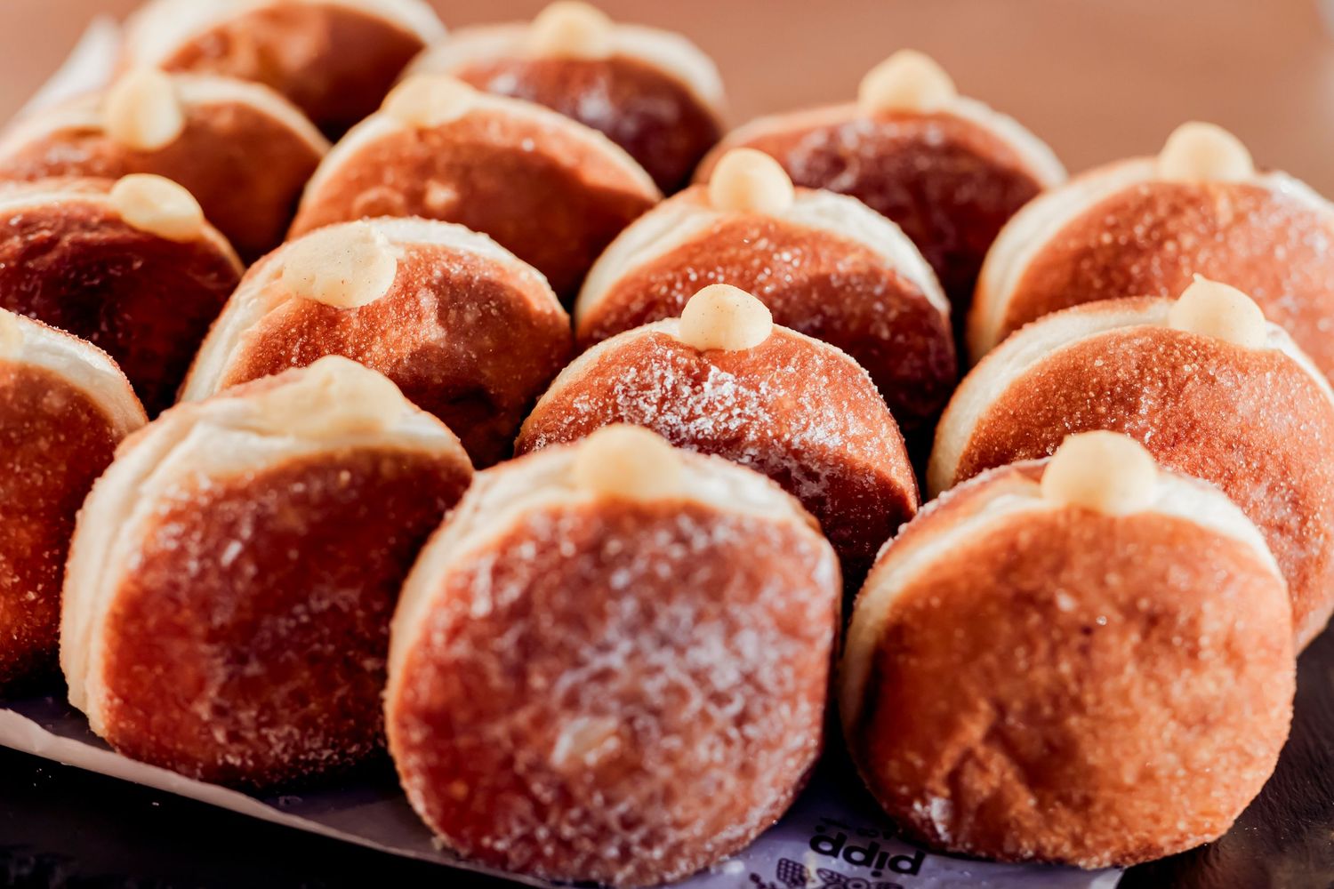 Close-up of freshly baked sugar-dusted round doughnuts filled with cream on a dark tray.
