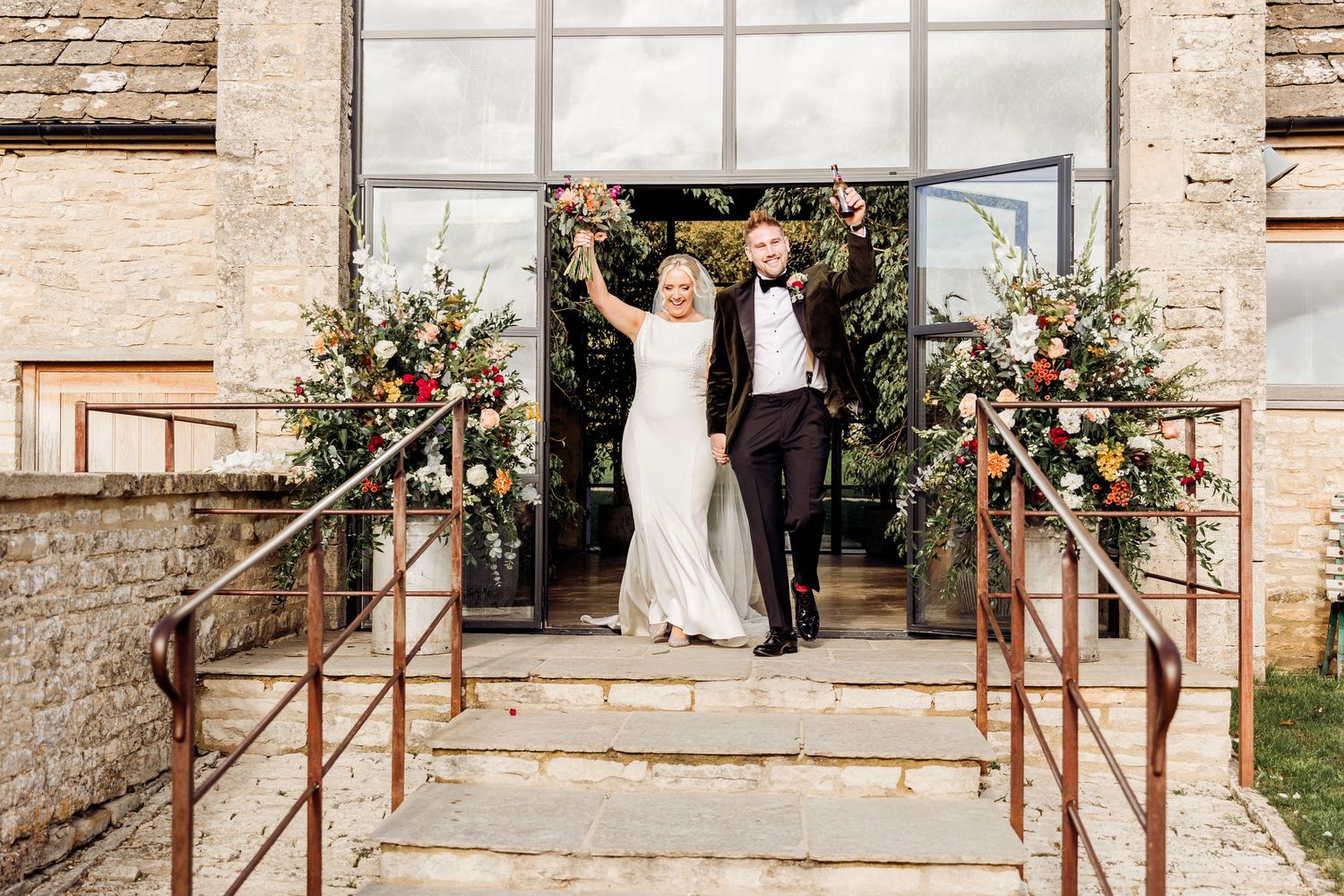 Joyful newlyweds celebrating at entrance of rustic wedding venue with floral arrangements.