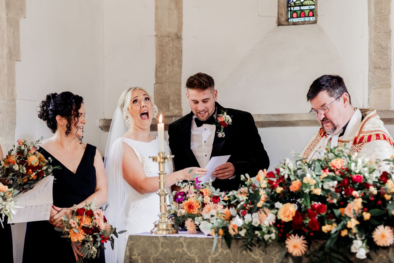 Bride laughing joyfully at the altar with groom, bridesmaid, and officiant during church wedding.