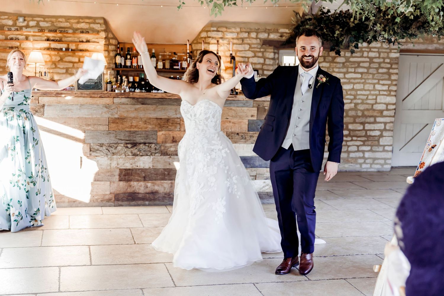Joyful bride and groom make grand entrance into rustic stone wedding reception venue to cheering guests.