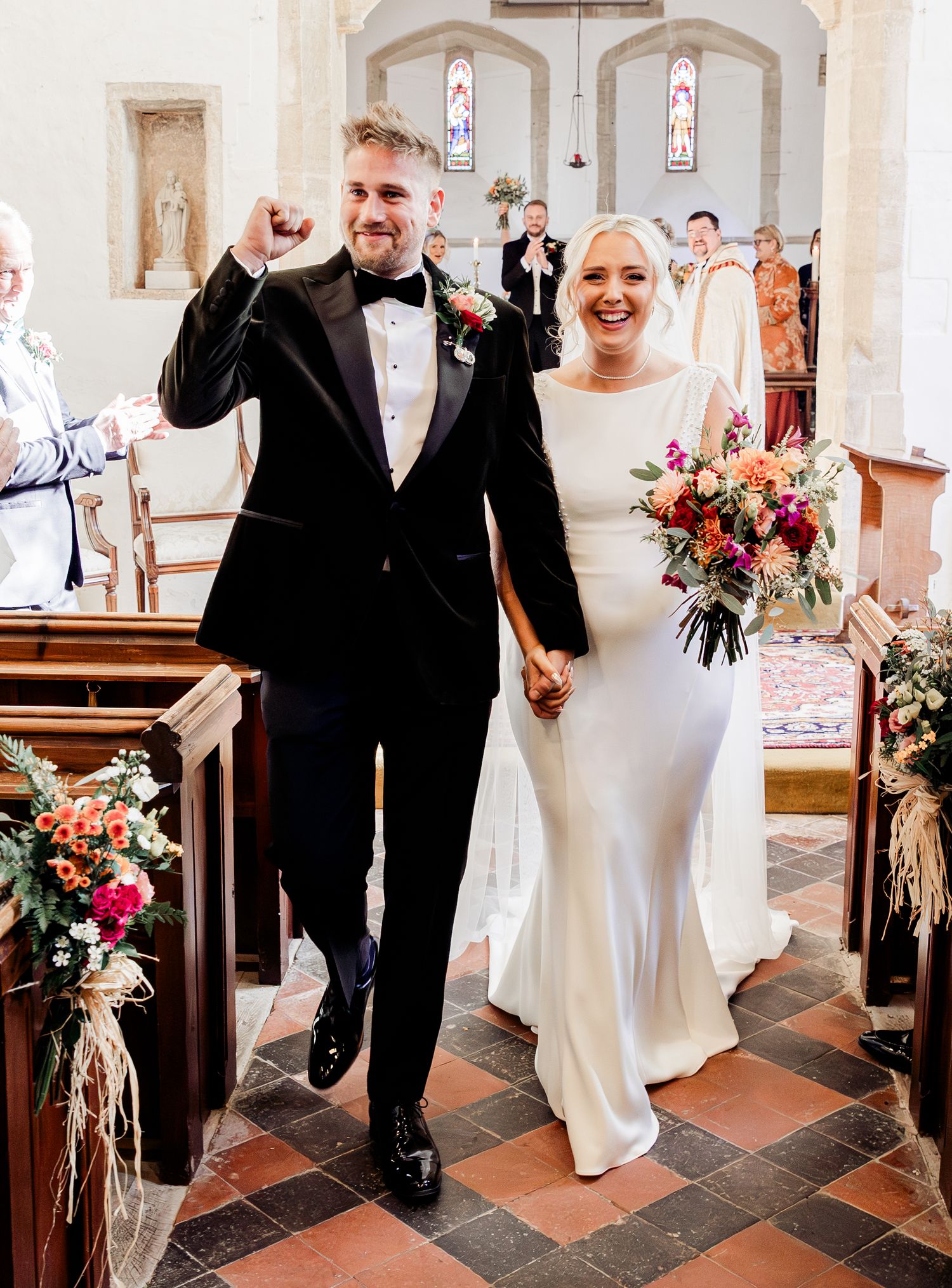 Jubilant groom pumps his fist as he walks down the aisle with his bride after their church wedding.
