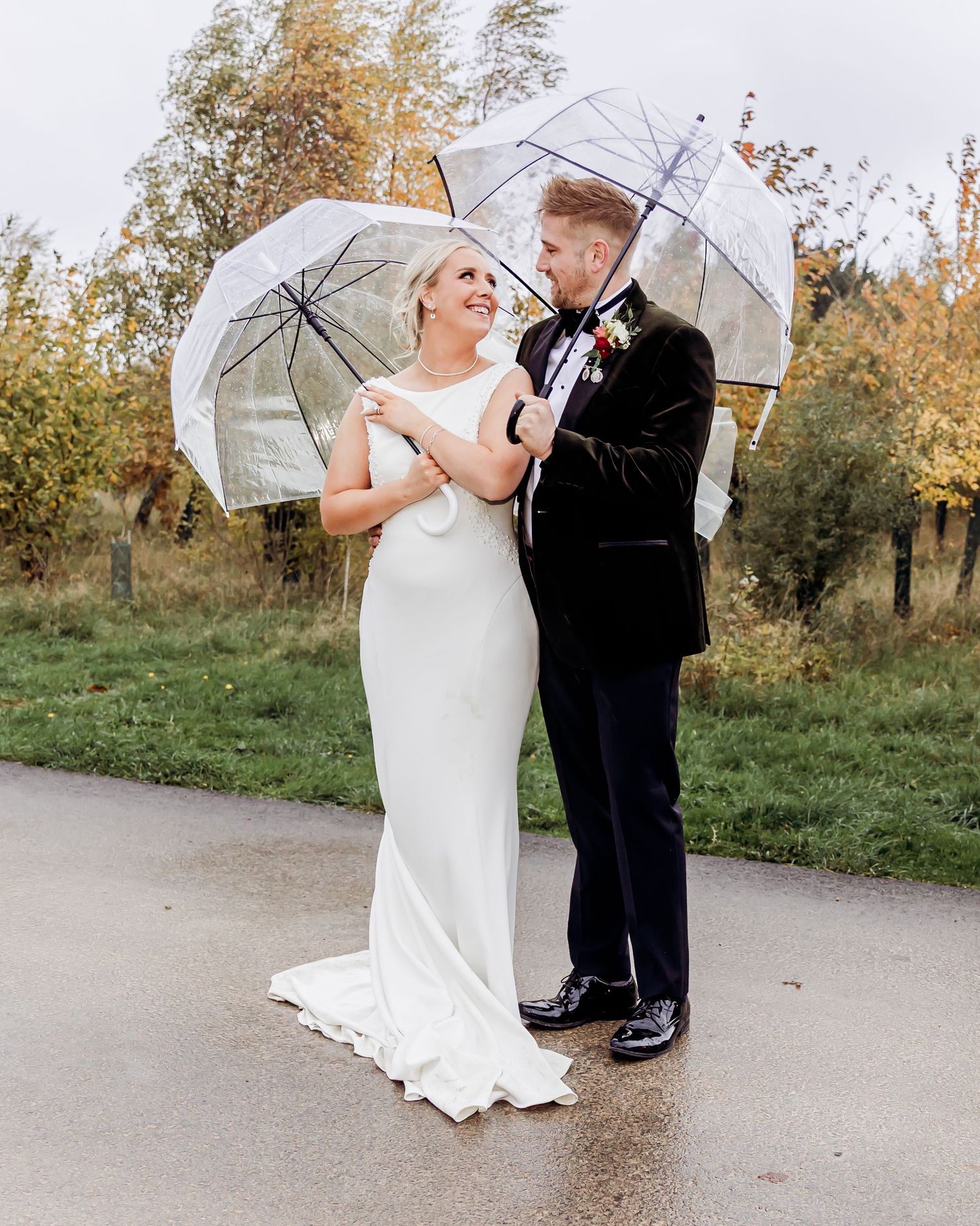 Bride and groom share a romantic moment under clear umbrellas on a rainy autumn day.