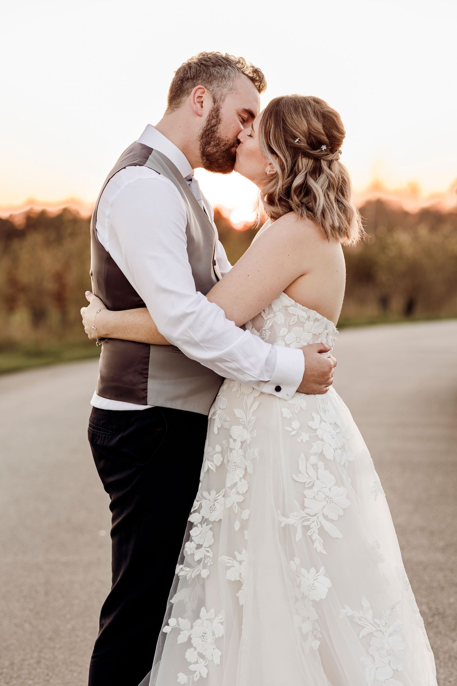 Bride and groom sharing a romantic kiss on a road at sunset.