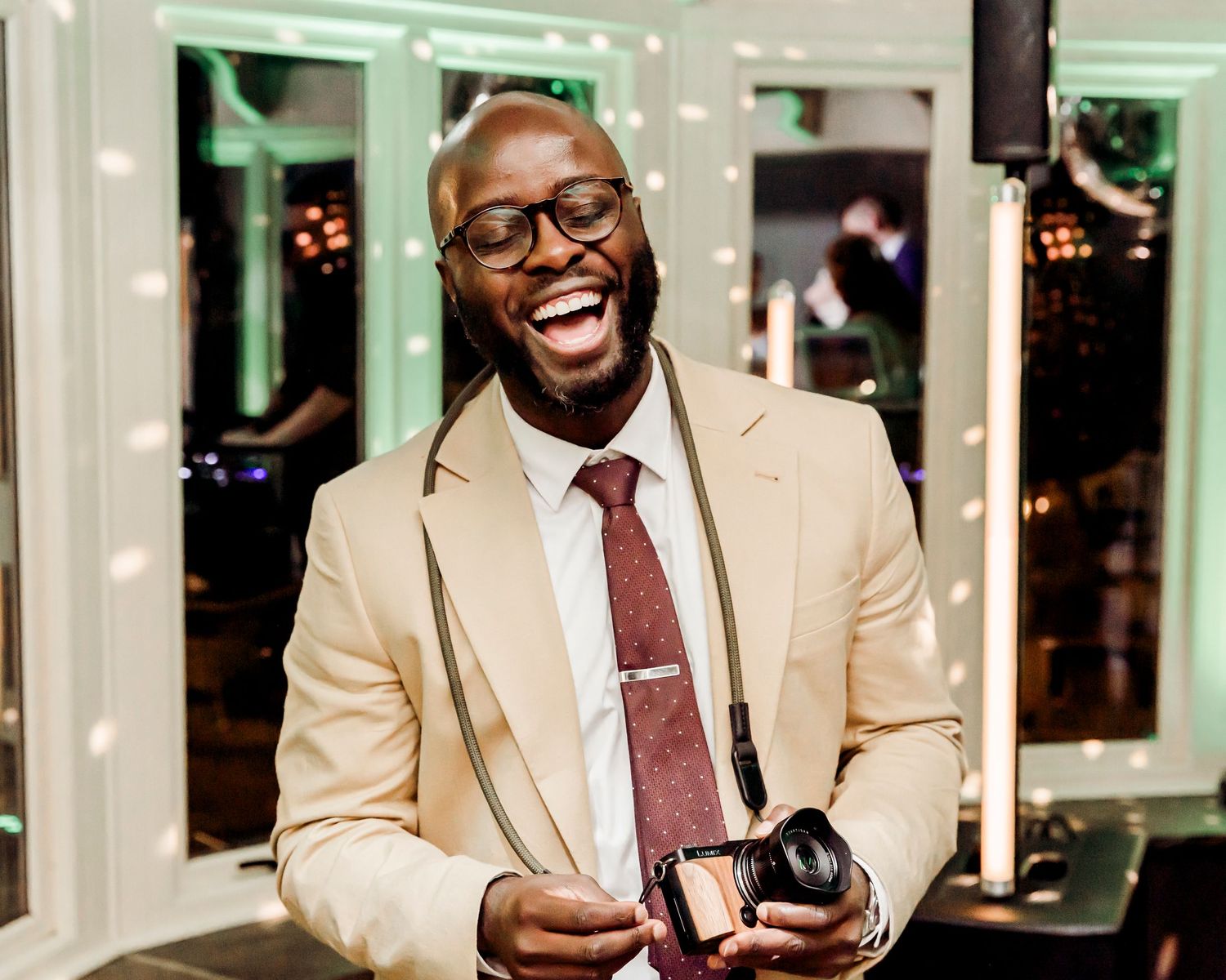 Smiling man in beige suit holding a camera at an elegant wedding reception venue.