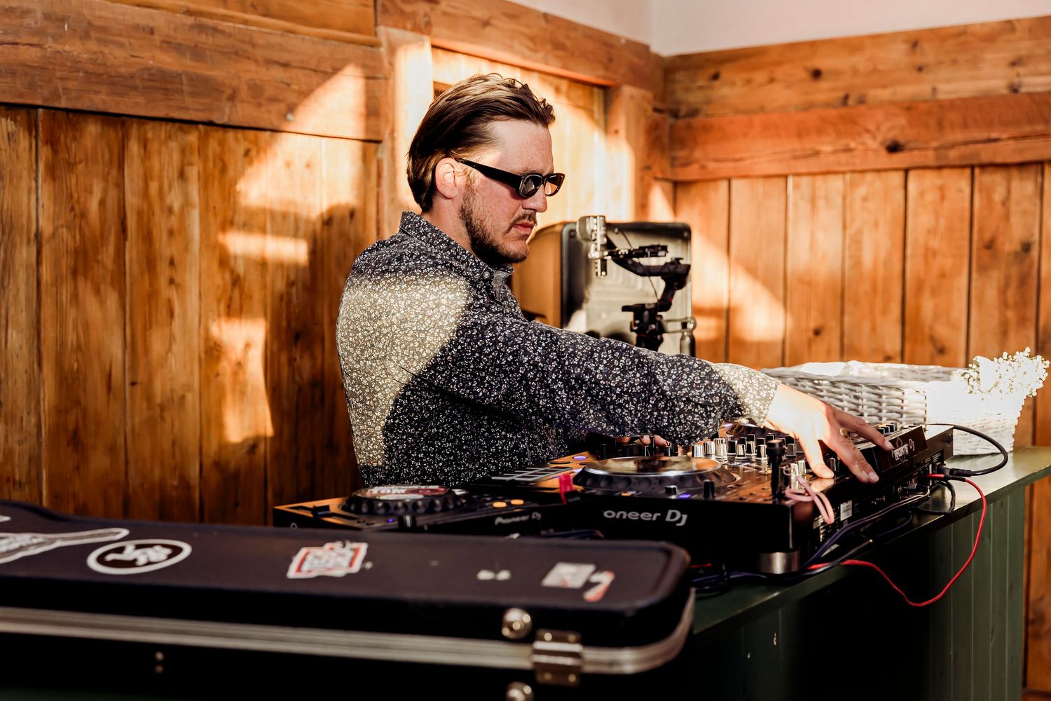 DJ wearing sunglasses performing at wedding reception in rustic wooden venue.