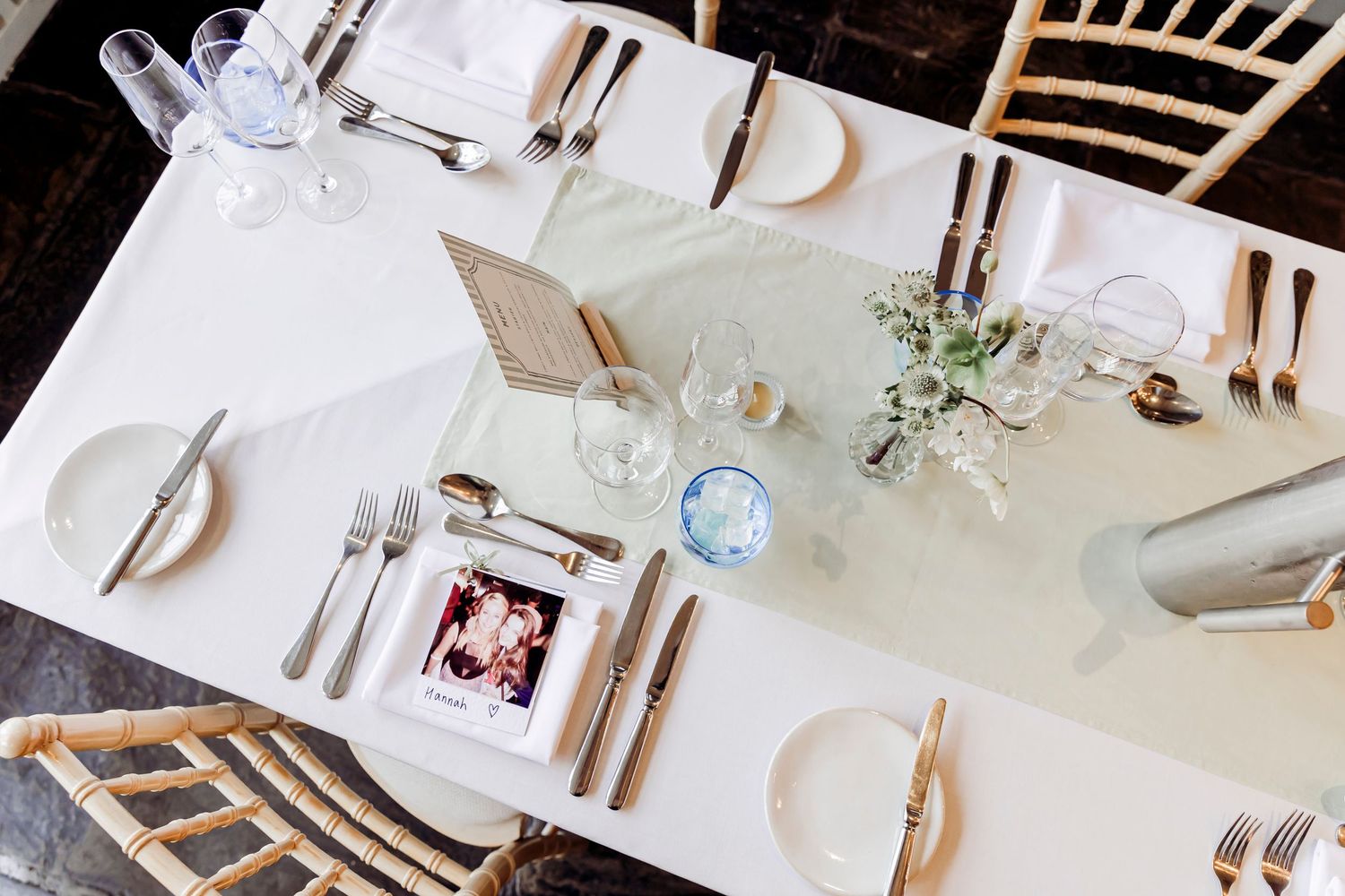 Elegant white wedding reception table set with gold cutlery, glassware, and floral decor.