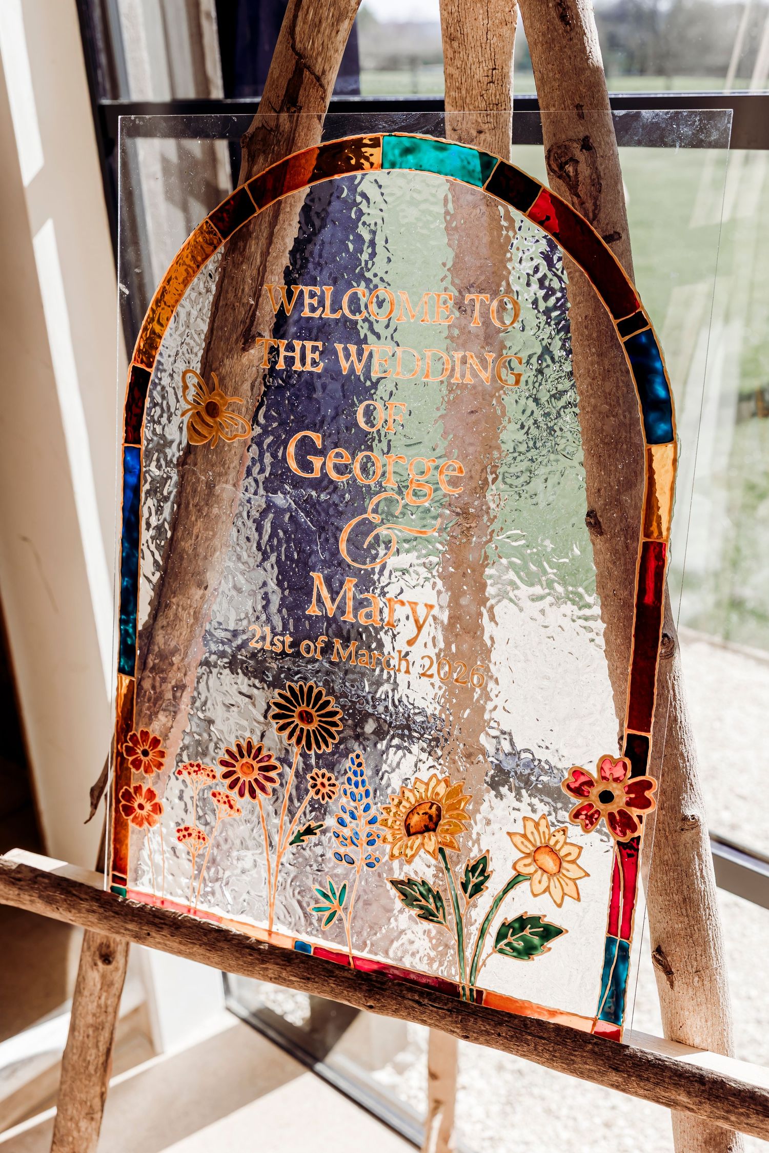 Decorative stained glass wedding welcome sign for George and Mary on a wooden easel by a window.
