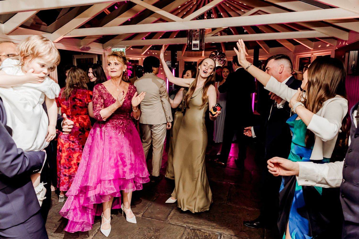 Wedding guests dancing energetically on the dance floor at evening reception.