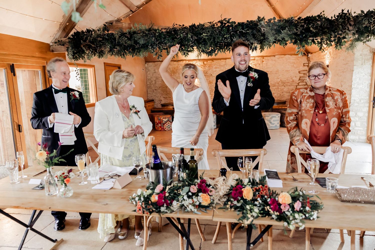 Bride and groom stand with family at a decorated wedding reception head table.