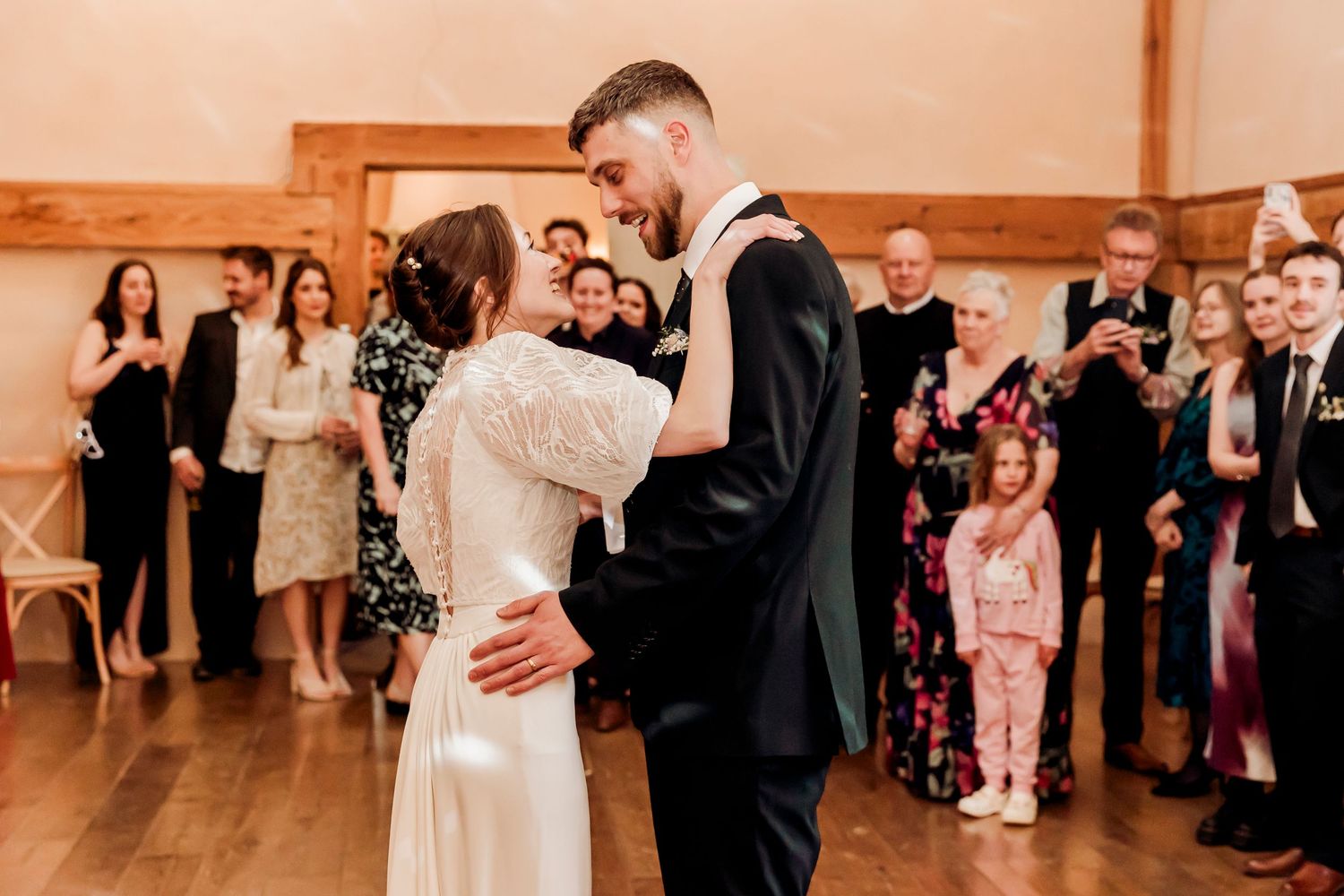 Bride and groom sharing first dance surrounded by wedding guests in rustic barn venue.