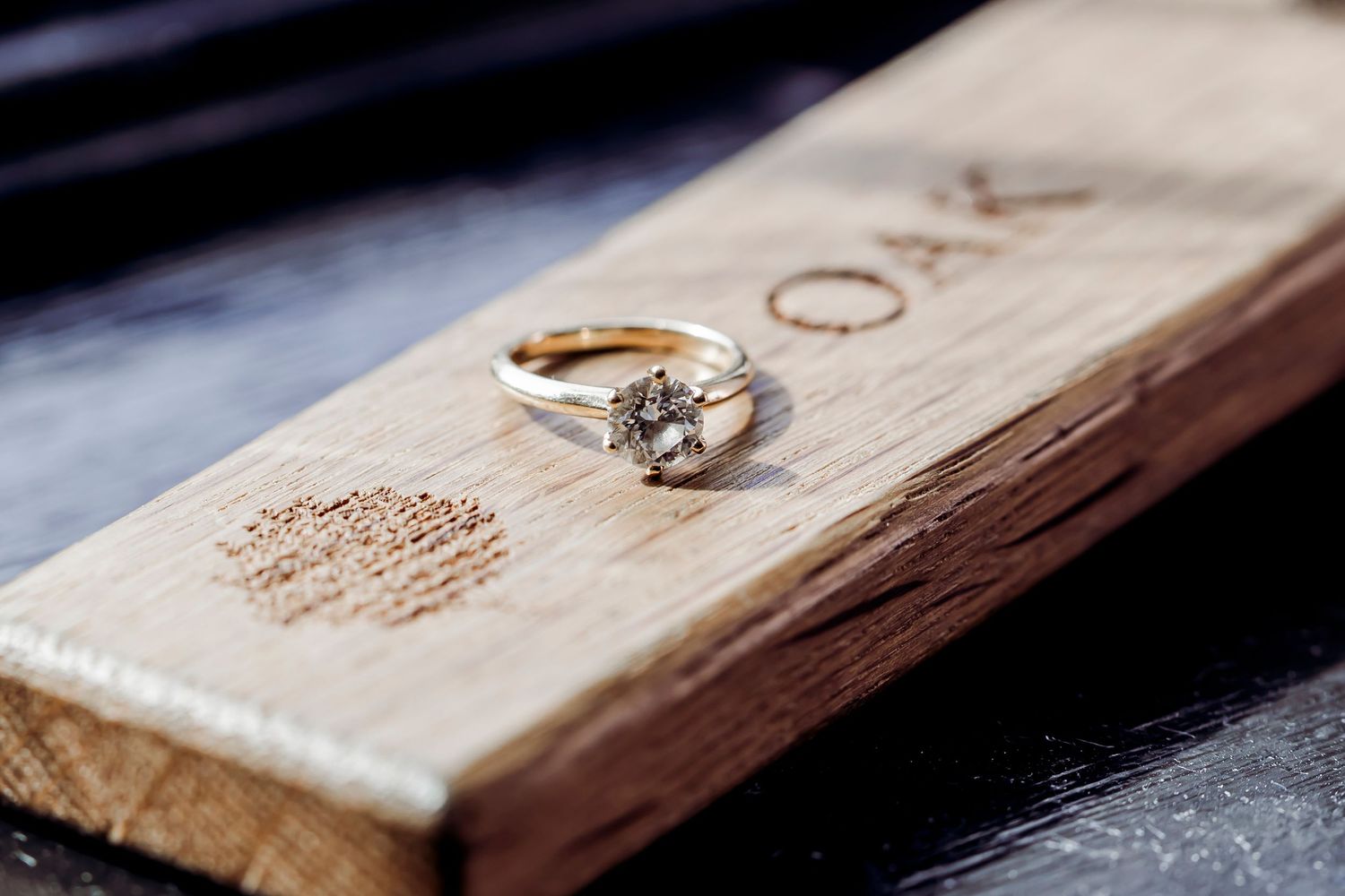Diamond solitaire engagement ring displayed on rustic oak wood block wedding detail shot.
