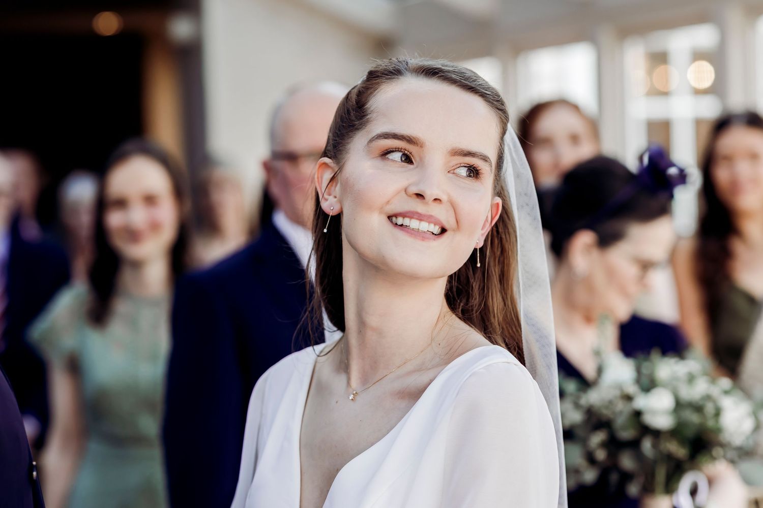 Smiling bride in white dress and veil looking up during wedding ceremony.