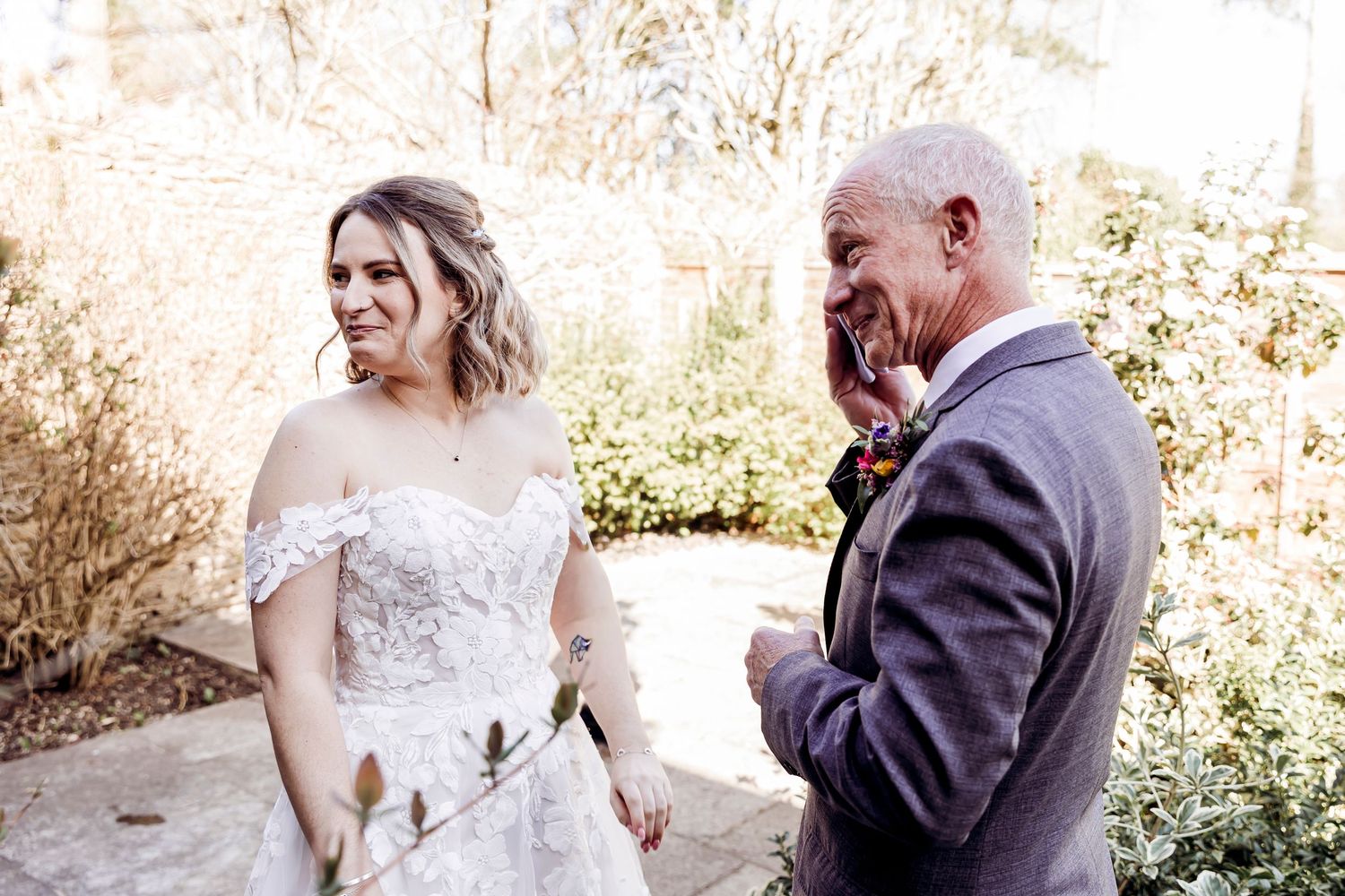 Emotional bride in off-shoulder lace gown shares a joyful moment with older gentleman at outdoor wedding ceremony.