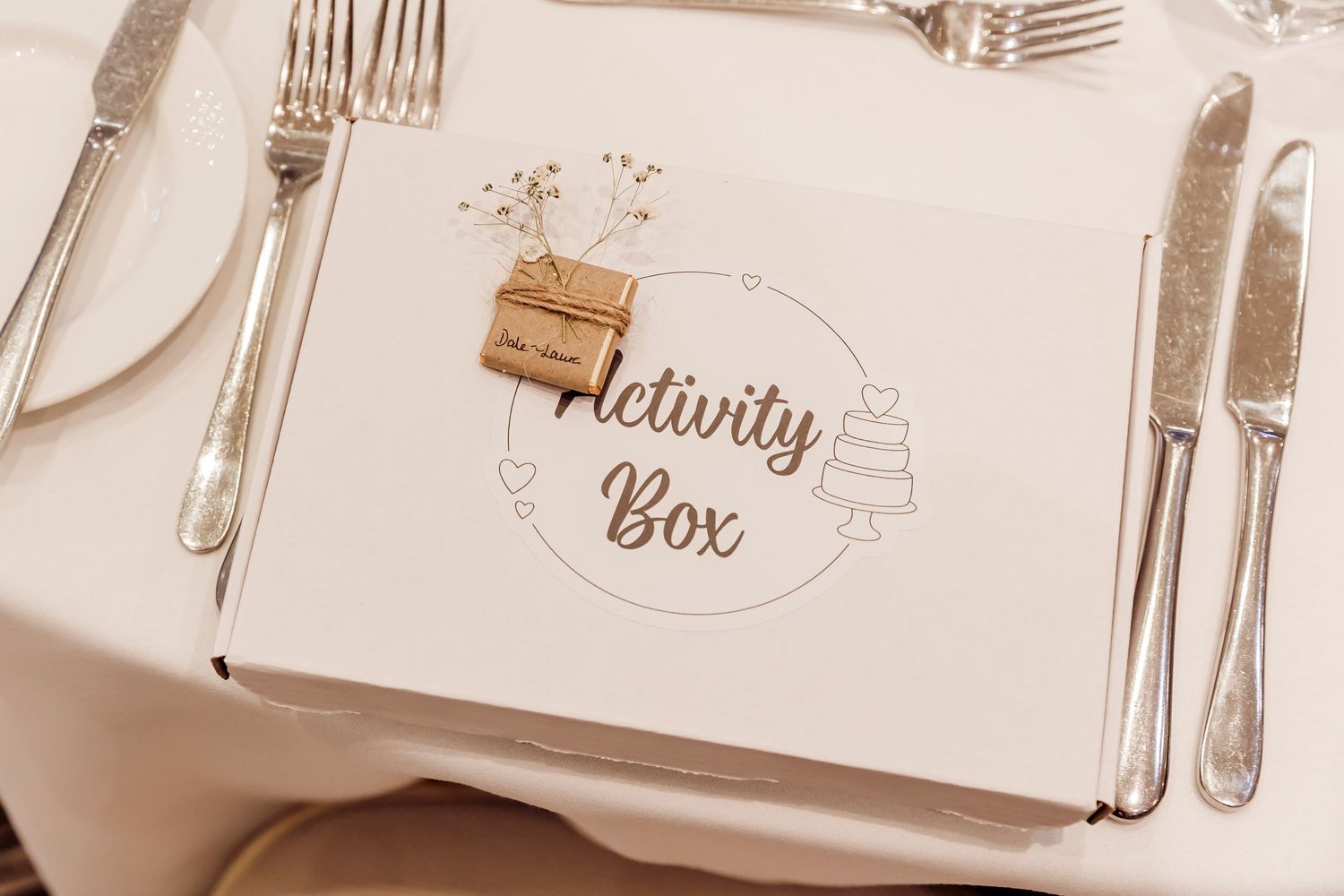 Elegant wedding activity box placed on a white place setting with silver cutlery at a reception dinner.