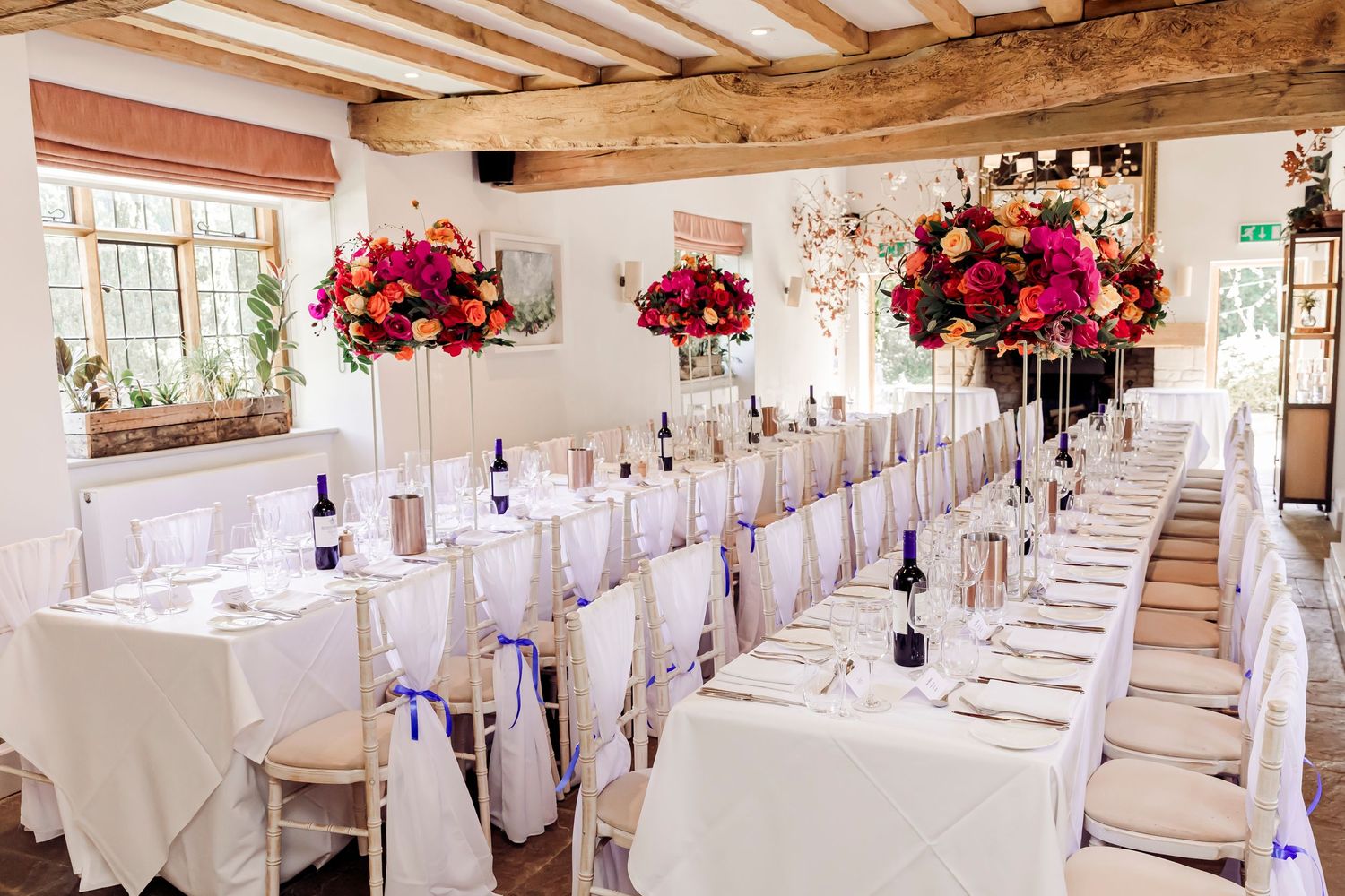 Elegant wedding reception hall with long white tables, floral centerpieces, and rustic beamed ceiling.