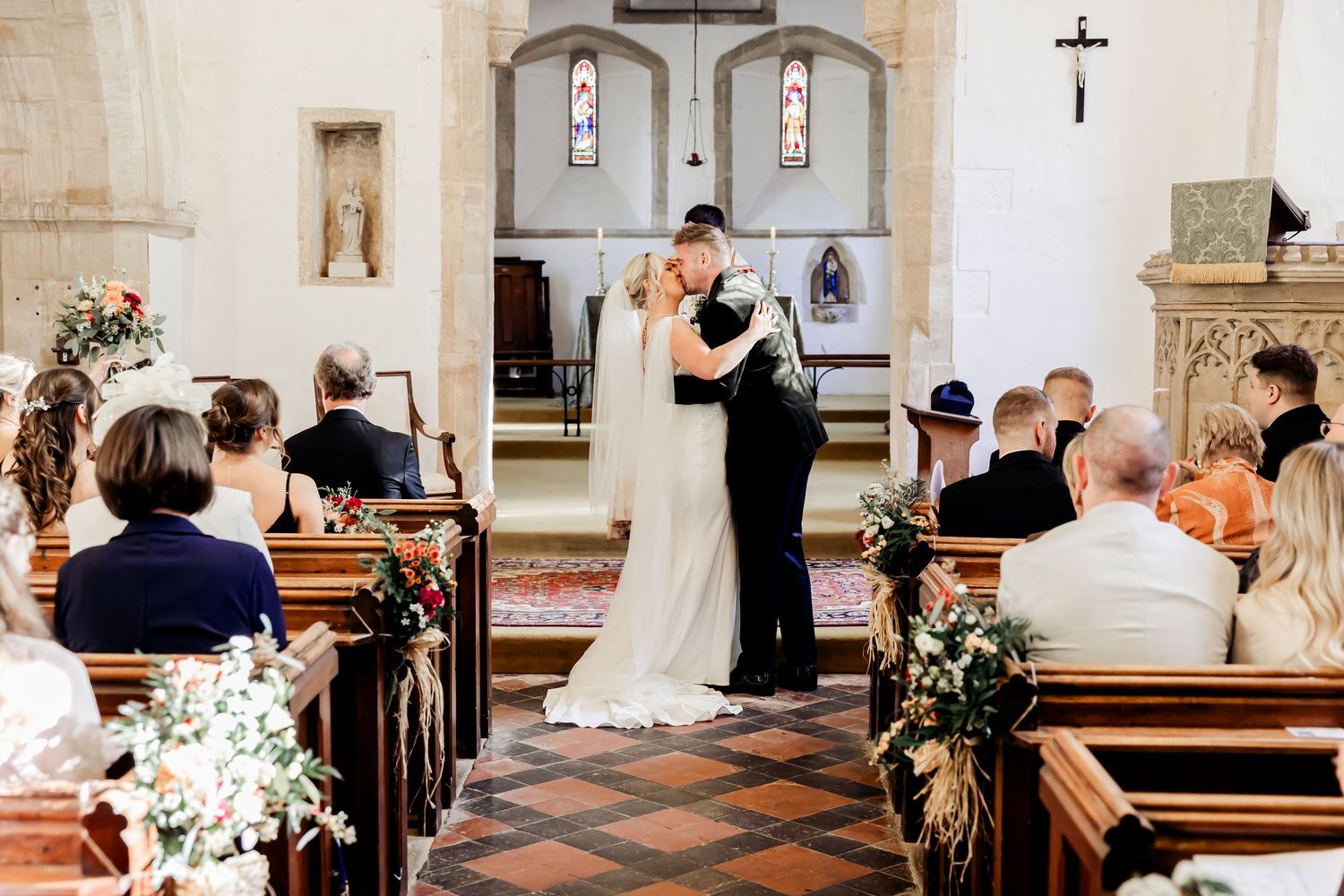 Newlyweds share their first kiss at the altar as wedding guests watch from wooden pews in a church.