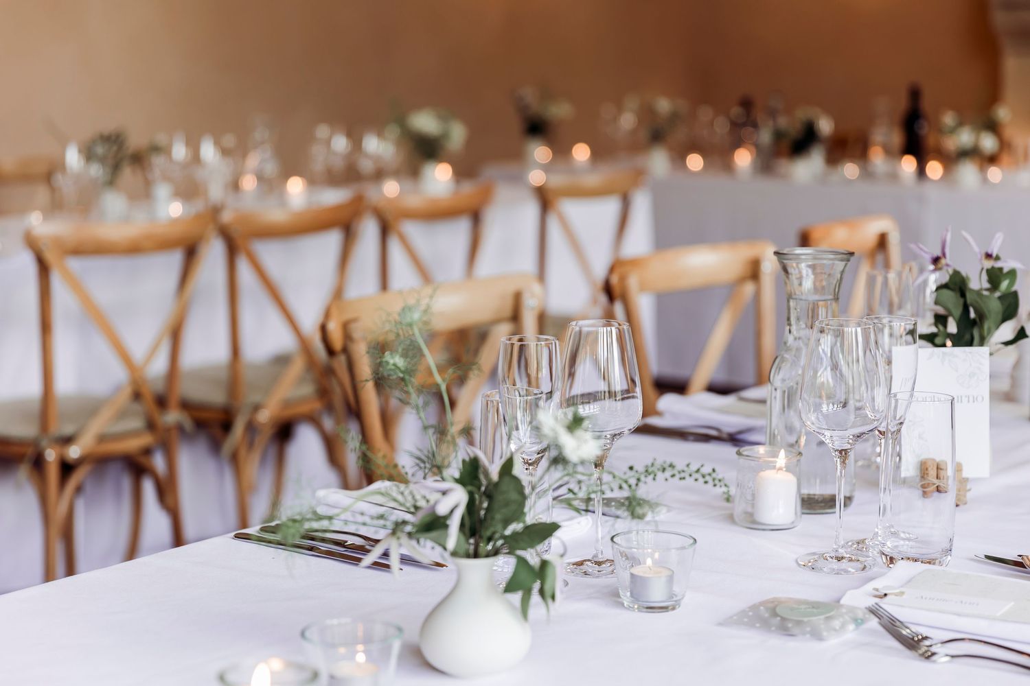 Elegant wedding reception table set with white linens, greenery, candles, and crystal glassware.