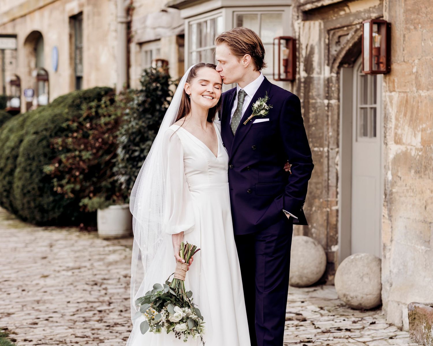 Elegant bride and groom posing together in a charming cobblestone courtyard setting.