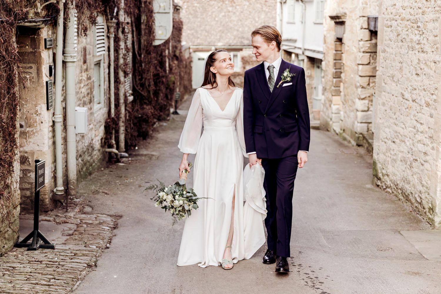 Bride and groom walk hand in hand down a charming cobblestone alley after wedding.