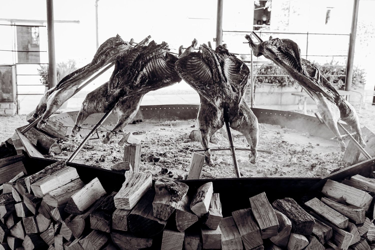 Black and white dramatic image of whole roasted bird over firewood in an outdoor cooking vessel.