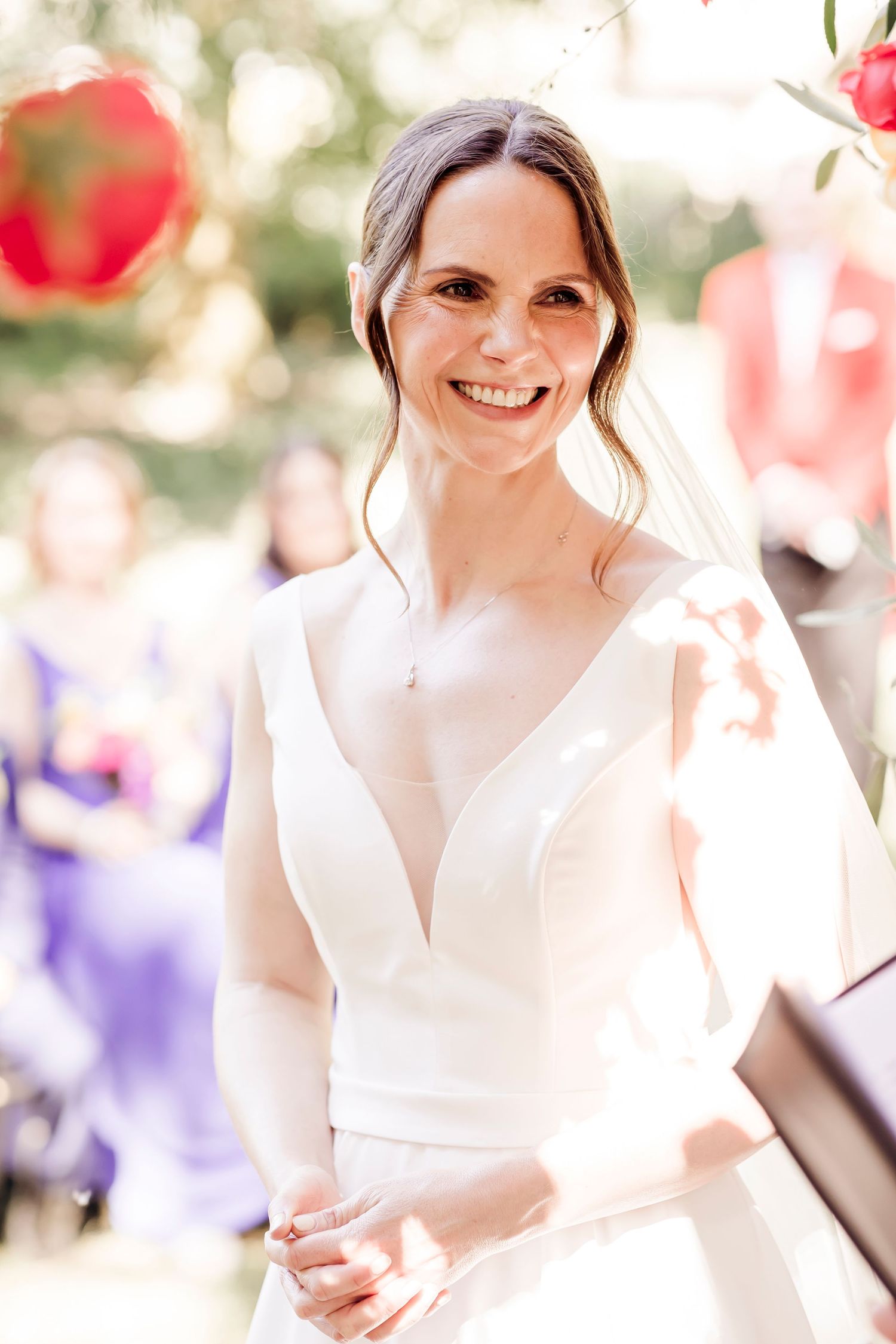 A radiant bride in a white V-neck gown smiling joyfully during her outdoor wedding ceremony.