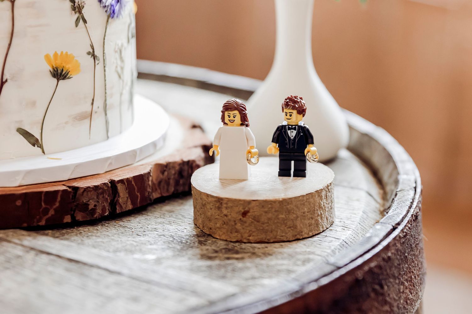 Cute LEGO bride and groom figurines displayed as wedding cake toppers on a wooden stand.