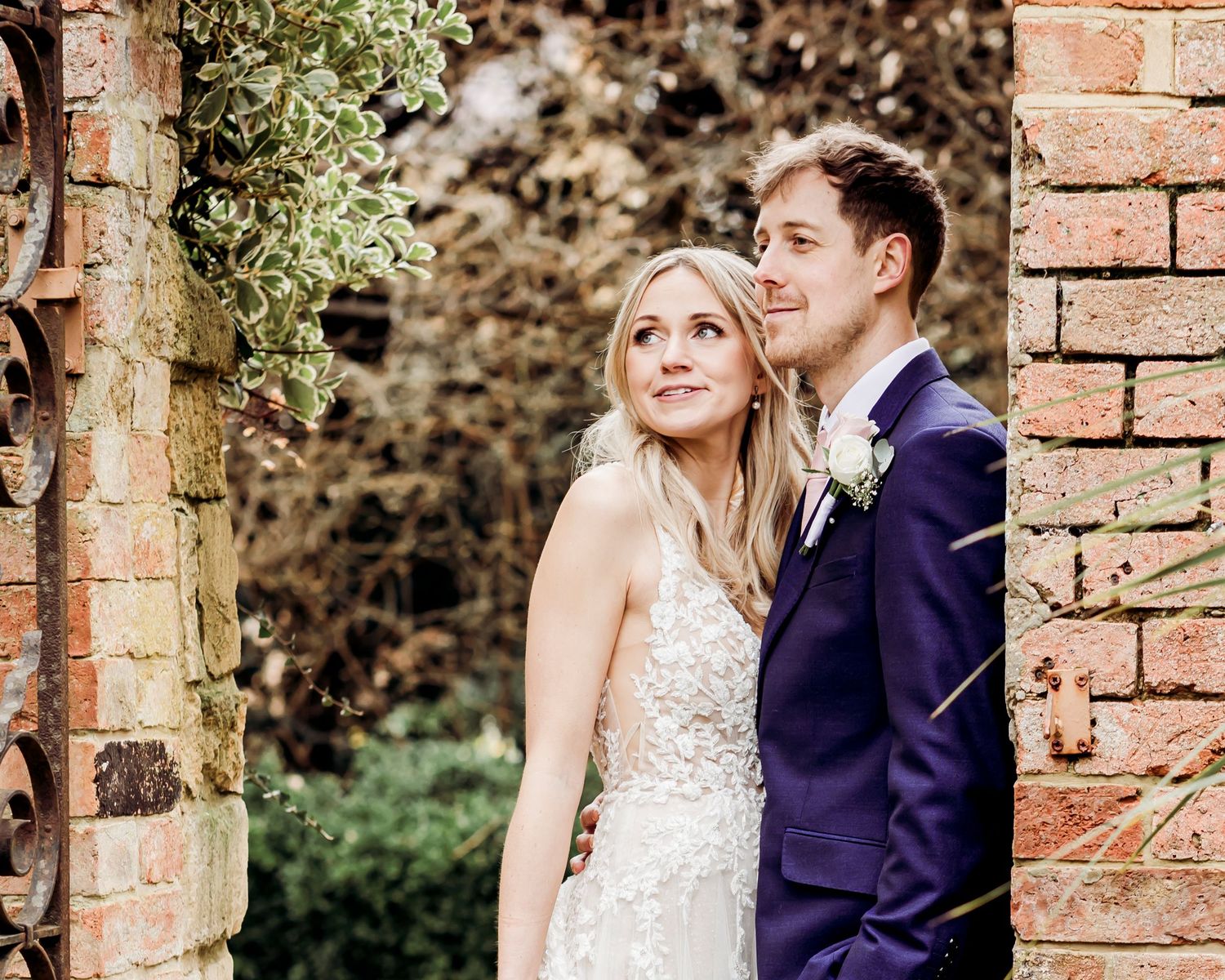 Bride and groom looking upward together romantically beside a moss-covered brick wall outdoors.