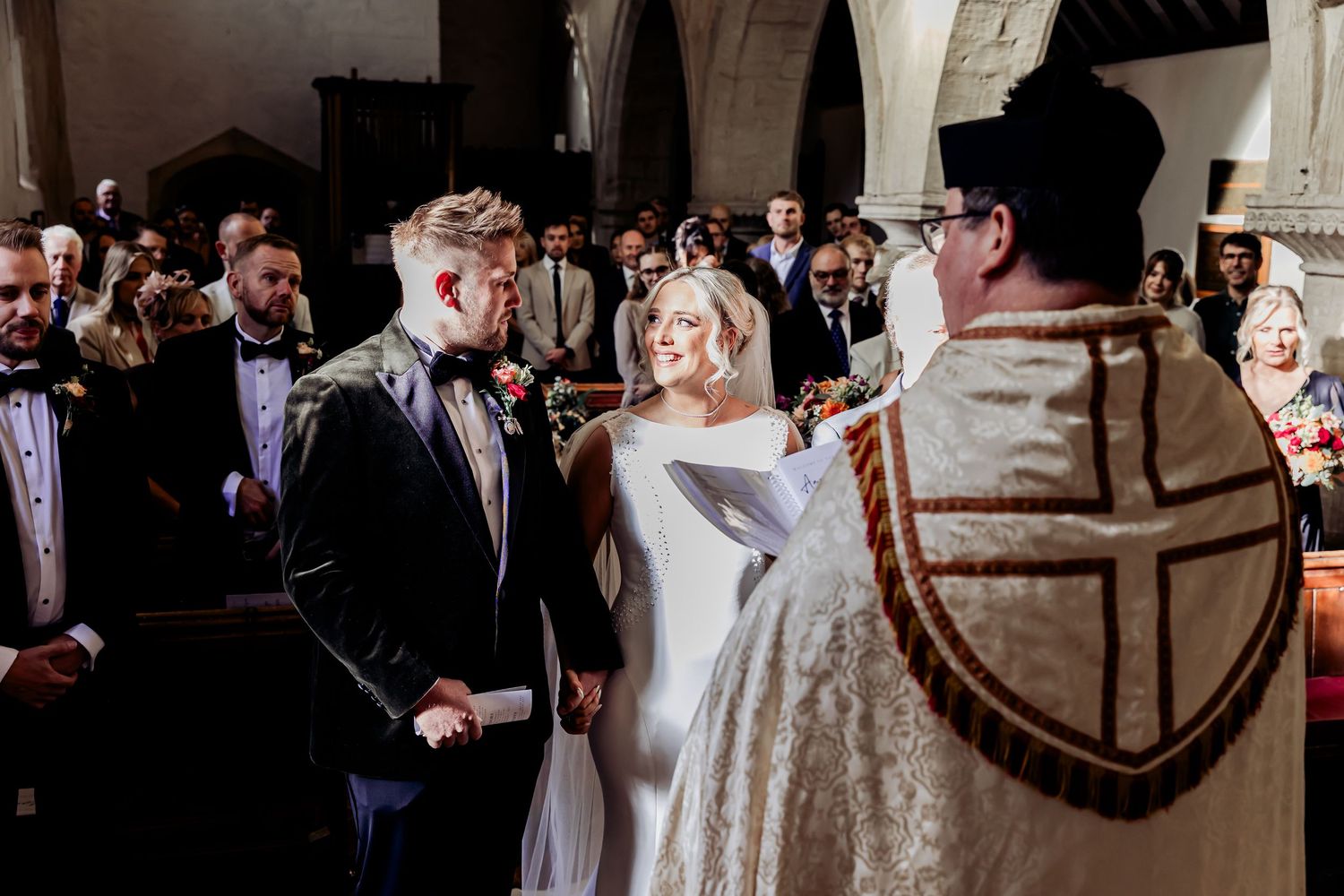 Bride and groom holding hands during wedding vows before officiant in a traditional church ceremony.