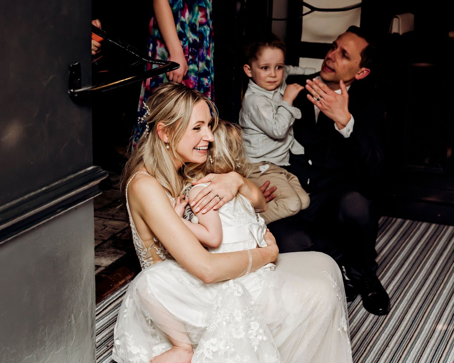 Emotional wedding moment as a bride in a lace gown hugs a young child at the reception.