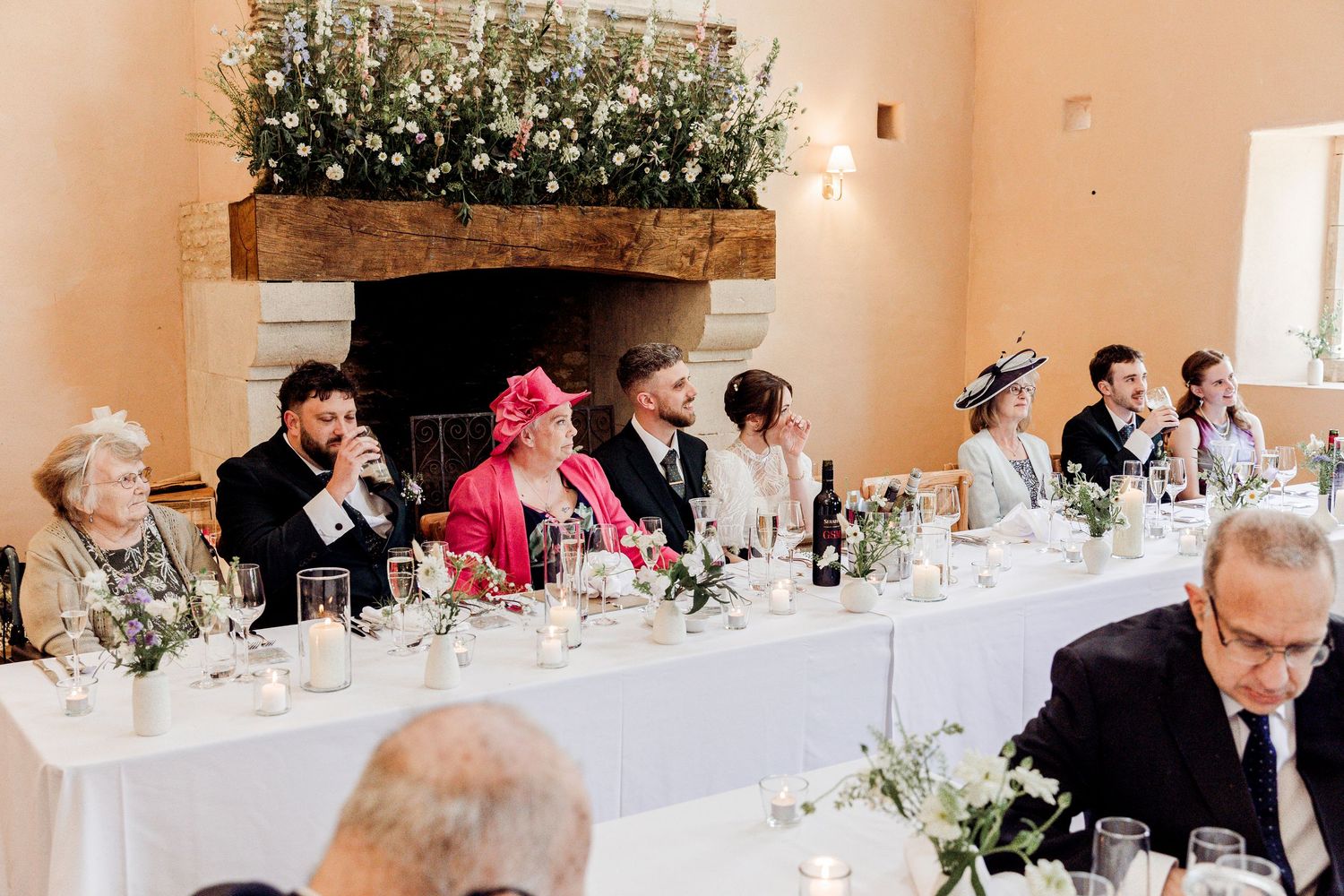 Wedding reception head table with guests seated before a floral fireplace.