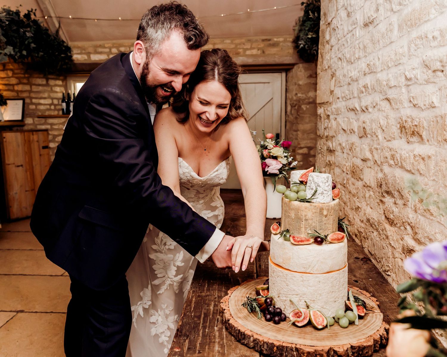 Smiling bride and groom cutting a rustic naked wedding cake on a wooden stand.