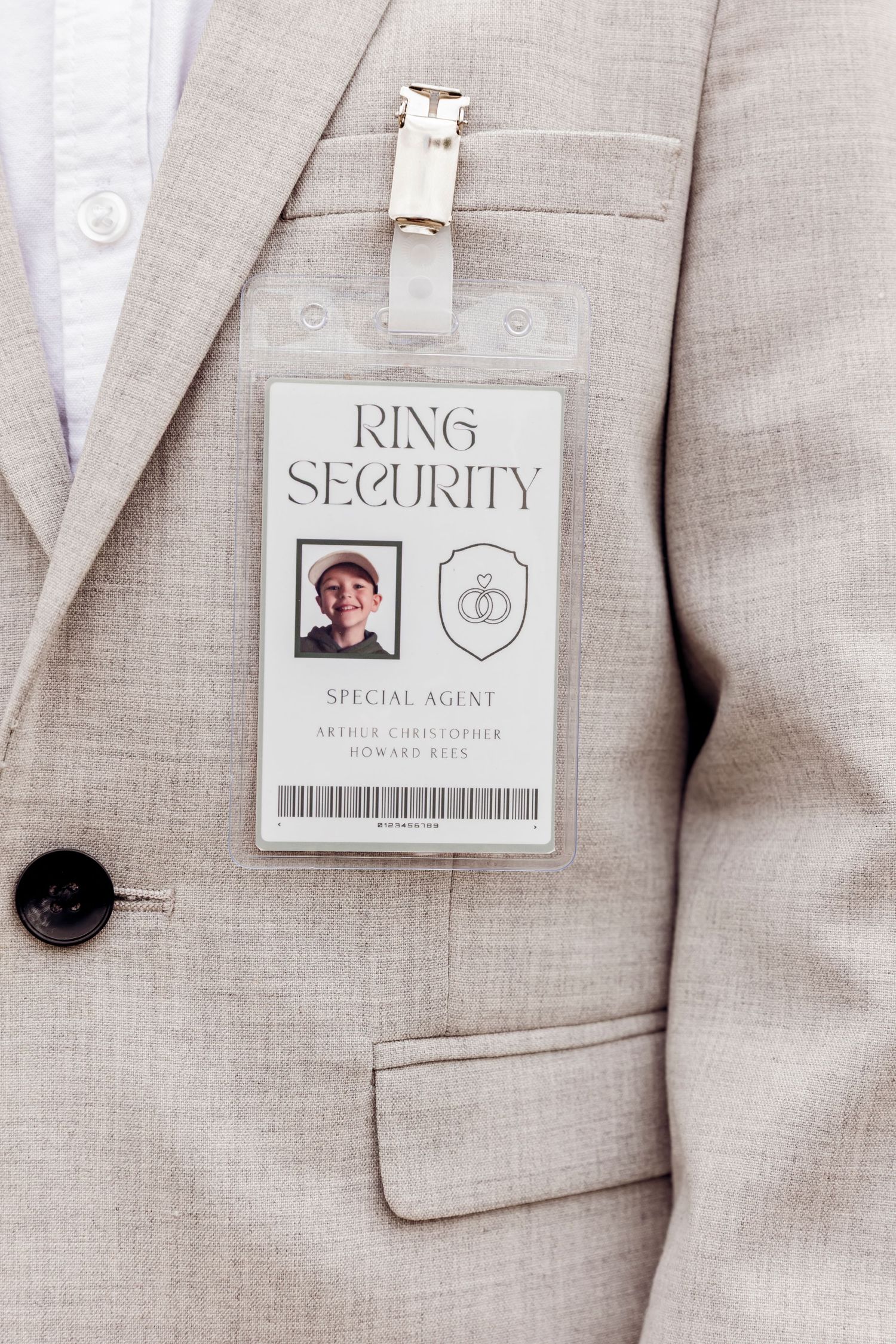 Ring security special agent badge pinned to a childs beige suit lapel at a wedding.