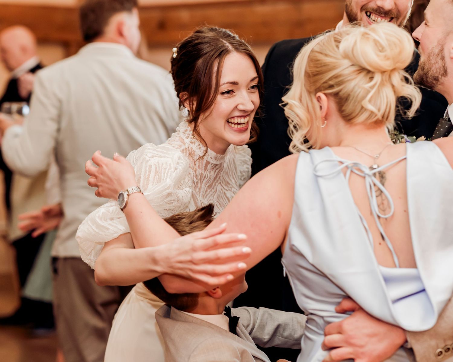 Joyful bride in lace wedding dress laughing and embracing guests on the dance floor at her wedding reception.